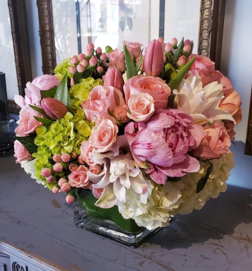 Spring in Paris - Transport yourself to a Parisian garden in springtime with this luxurious, romantic arrangement. Designed in a modern clear glass cube, it features a lush blend of soft white and green hydrangeas, fragrant pink garden roses, delicate peonies, elegant lilies, and blush spray roses. Accents of pink hypericum berries and artfully wrapped aspidistra leaves complete this fresh, feminine design—perfect for celebrating love, beauty, and new beginnings. One of our most-loved arrangements.  Please note: Seasonal flowers may vary based on availability, ensuring each arrangement is unique and fresh.  Freshness Guarantee: We stand behind our quality. Your flowers are guaranteed to look fresh and beautiful for 3–5 days from delivery.  To help them last:  •Top off the vase with clean water daily.  •Keep arrangements away from direct sun, heat, and drafts.  •Trim stems slightly after a couple of days if possible.