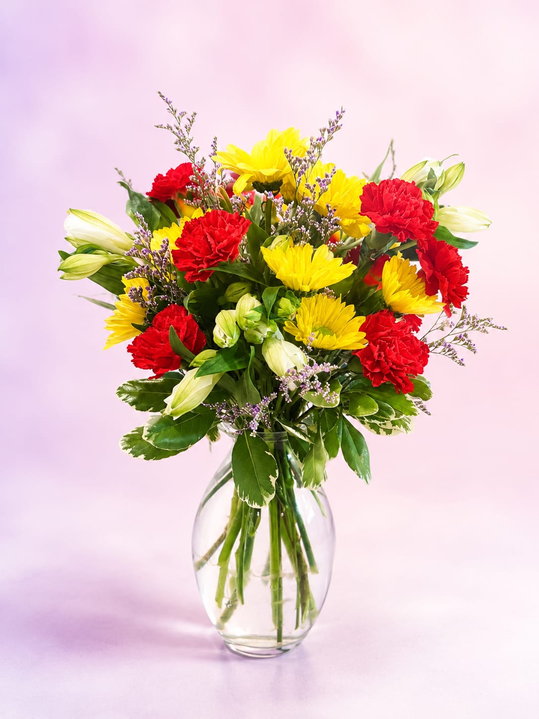 Crimson &amp; Sunshine - Bold, bright, and full of joyful energy, Crimson &amp; Sunshine is a vibrant arrangement designed to make every day feel a little more special. Rich crimson carnations and sunny yellow daisy mums are beautifully complemented by elegant white alstroemeria, airy lavender statice, and lush variegated greenery, all gathered in a classic clear glass vase.  With its cheerful blend of warm colors and fresh textures, this bouquet brings together timeless beauty and everyday happiness. Whether celebrating a birthday, sending encouragement, expressing gratitude, or simply brightening someone's day, Crimson &amp; Sunshine delivers a heartfelt touch that's sure to make them smile.