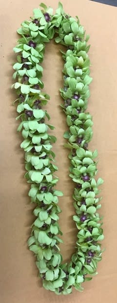 A green floral lei with small purple accents laid on a plain surface