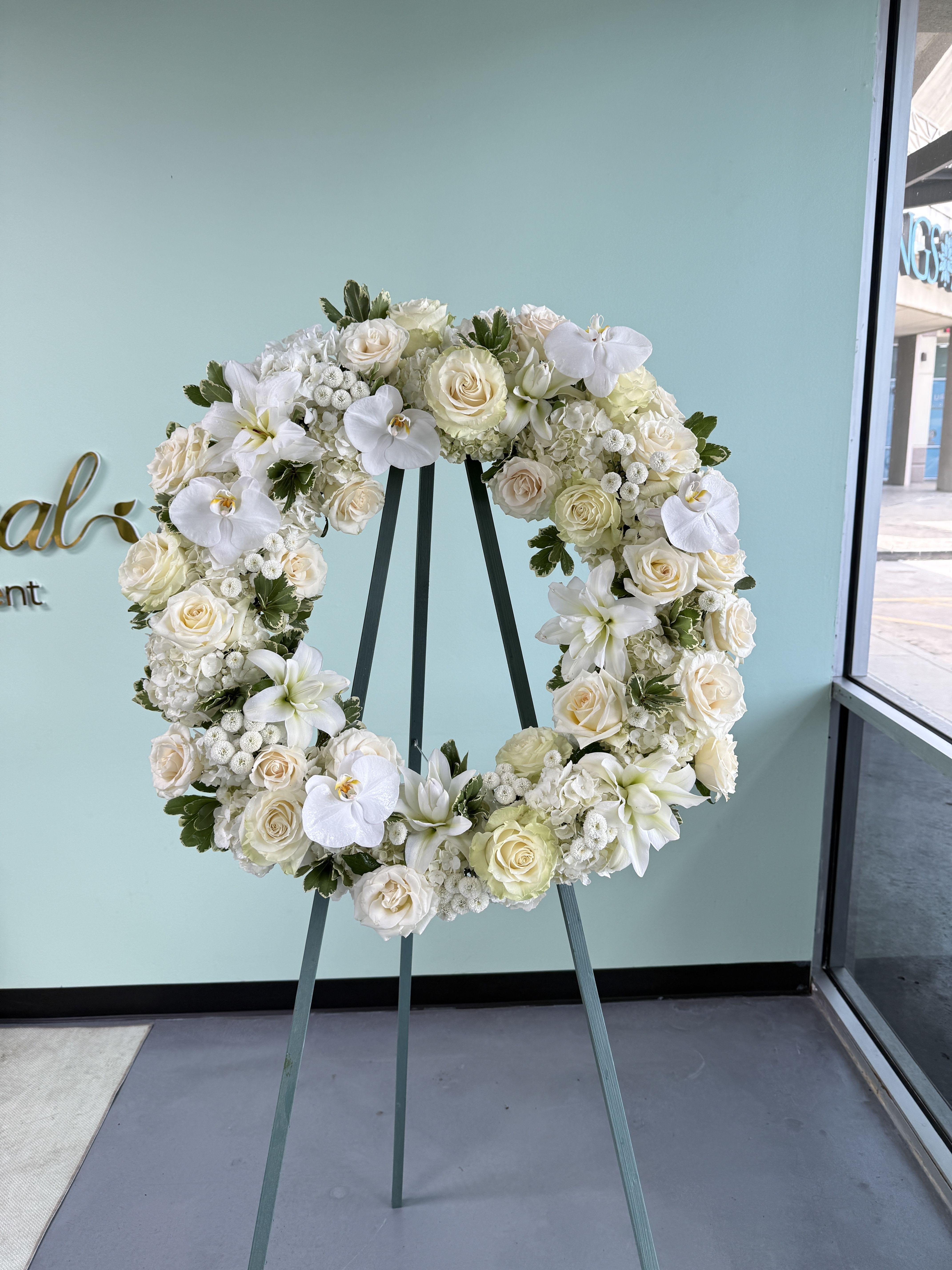 Sympathy Wreath Circle 01 - White rose, orchid and hydrangea wreath with soft accents on a tall metal easel-elegant, serene sympathy display in white and green for memorials or formal services.