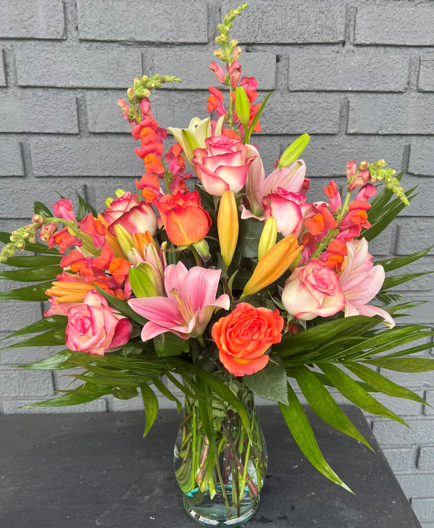 Mixed bouquet of pink roses, lilies, and orange snapdragons in a glass vase