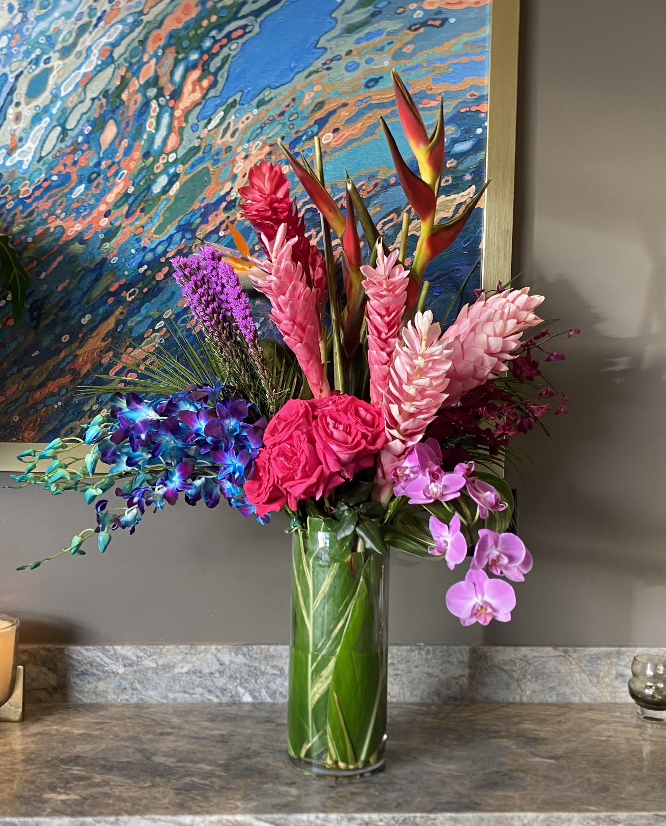 Tropical bouquet in a tall glass vase with pink orchids and bright mixed blooms