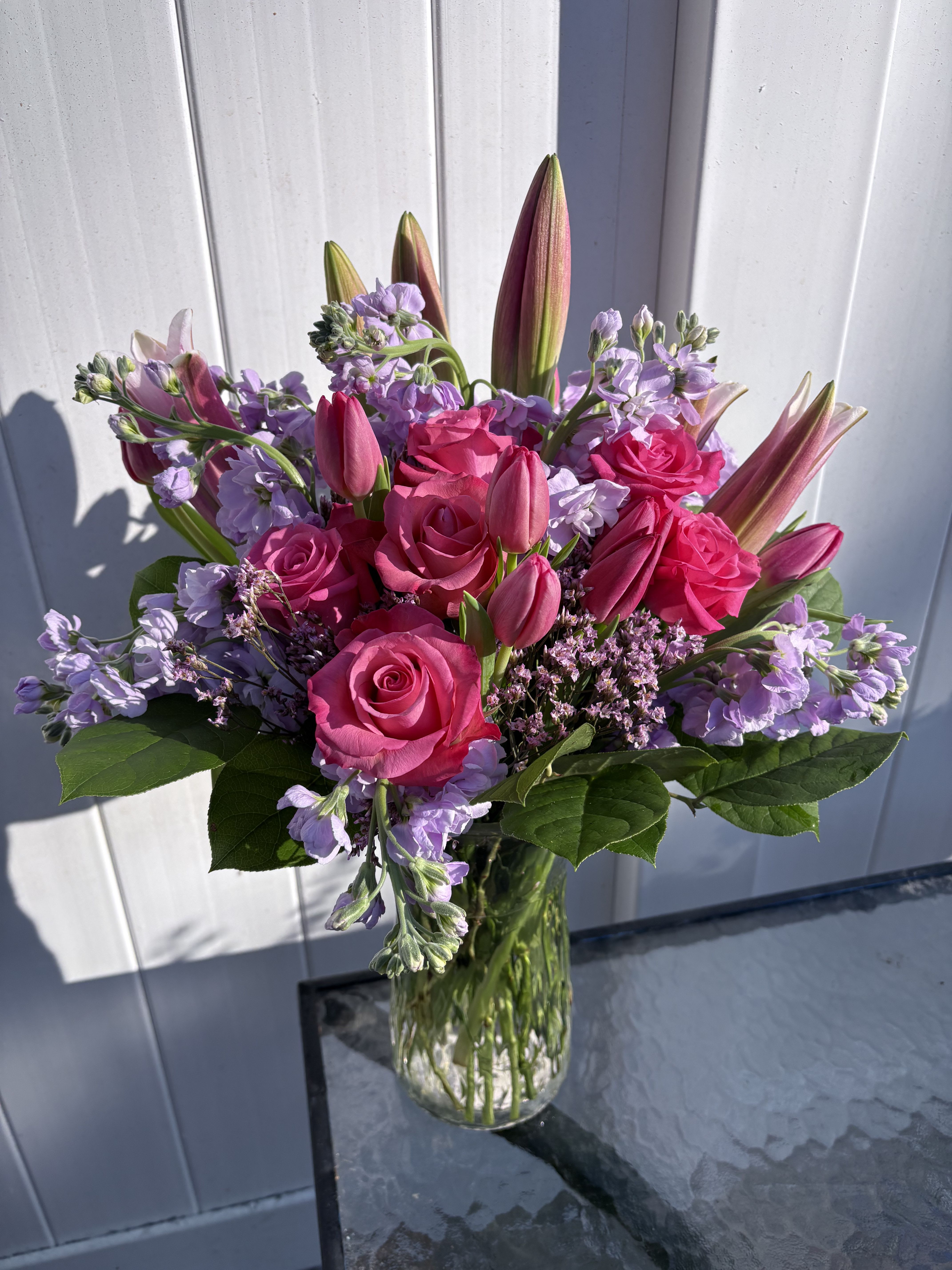 Pink roses and lilies arranged in a clear glass vase with lavender flowers