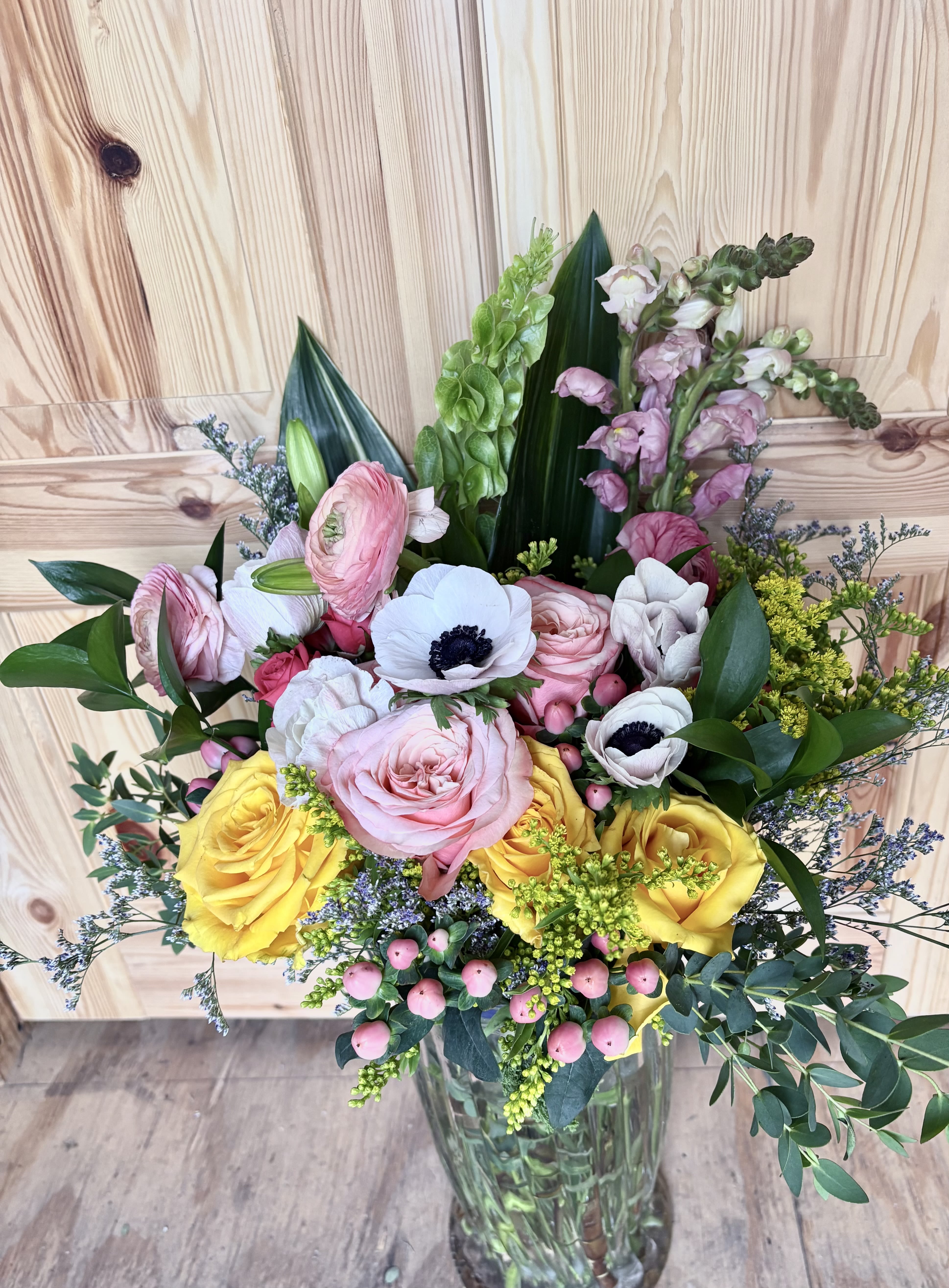Better days  - Large pink and yellow roses mingle with white anemones and tall pink snapdragon spikes to create a garden-style birthday bouquet that feels both celebratory and elegant. The soft pastel palette-blush pinks and creams-brightens with sunny yellow accents, so the person you're thinking of will feel noticed and cheered whether this marks a birthday, a thank-you, or a springtime moment.  The arrangement layers full roses, delicate anemone faces, and vertical snapdragon stems for height and movement, with small berry-like accents and airy filler flowers adding texture and a natural, hand-gathered look. Sturdily arranged in a clear glass vase, it arrives ready to display on a dining table or entry console; the classic vase keeps the focus on the blooms and their fresh colors.  Perfect for moms, friends, or coworkers who appreciate a refined yet joyful bouquet, this design reads as thoughtful and uplifting. Standard care-fresh water and a cool spot away from direct heat-will help the flowers last, and choosing delivery ensures it arrives ready to make someone feel genuinely celebrated.