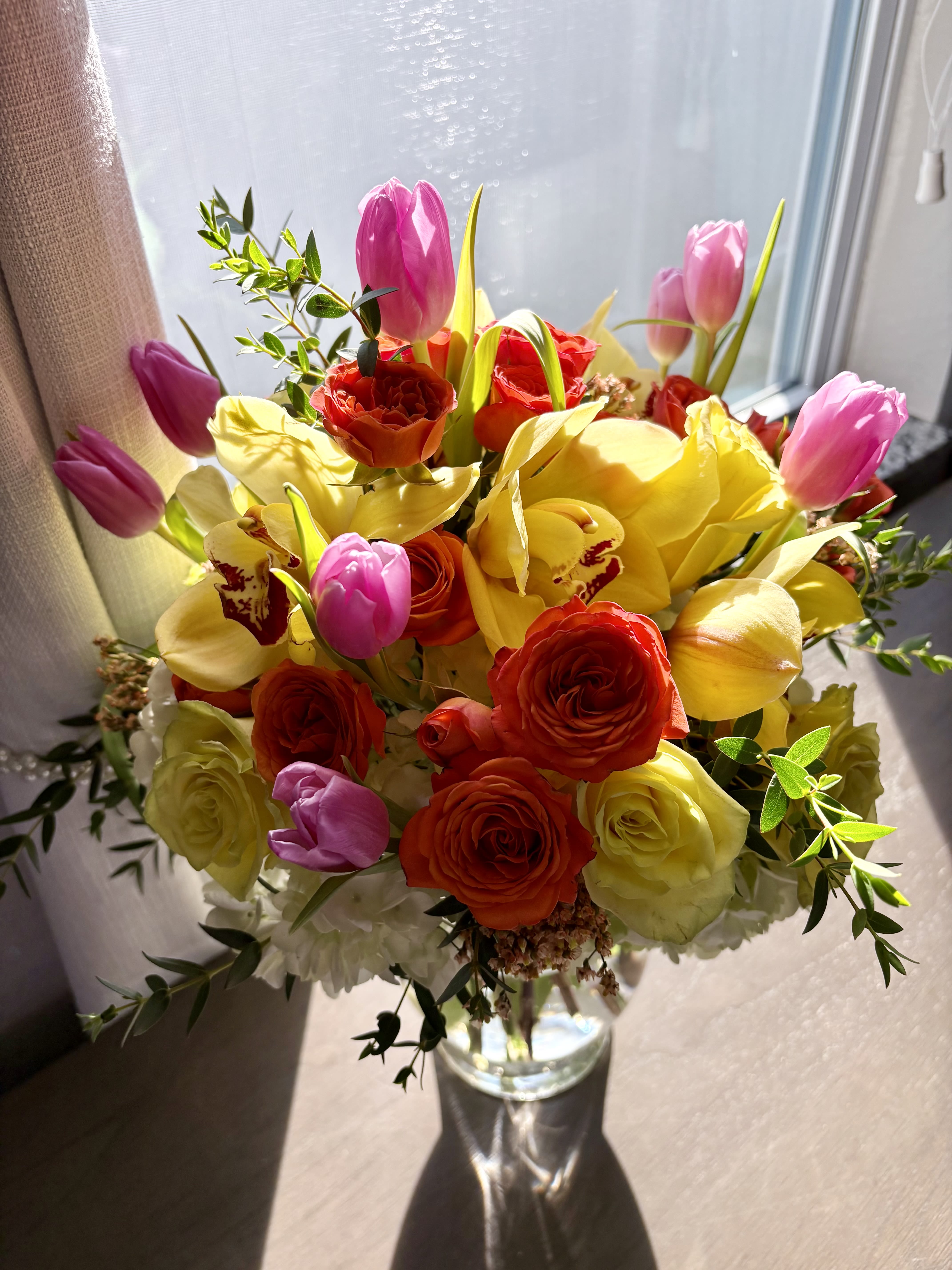 Bouquet of pink tulips, yellow orchids, and red roses in a glass vase