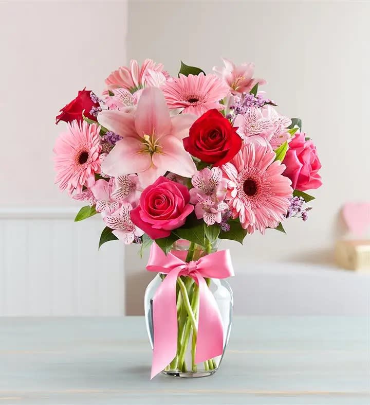 Pink and red mixed flowers in a glass vase with a pink ribbon