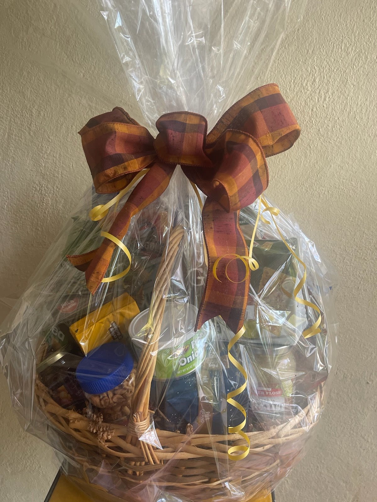 Gift basket wrapped in cellophane with a plaid bow and assorted snacks