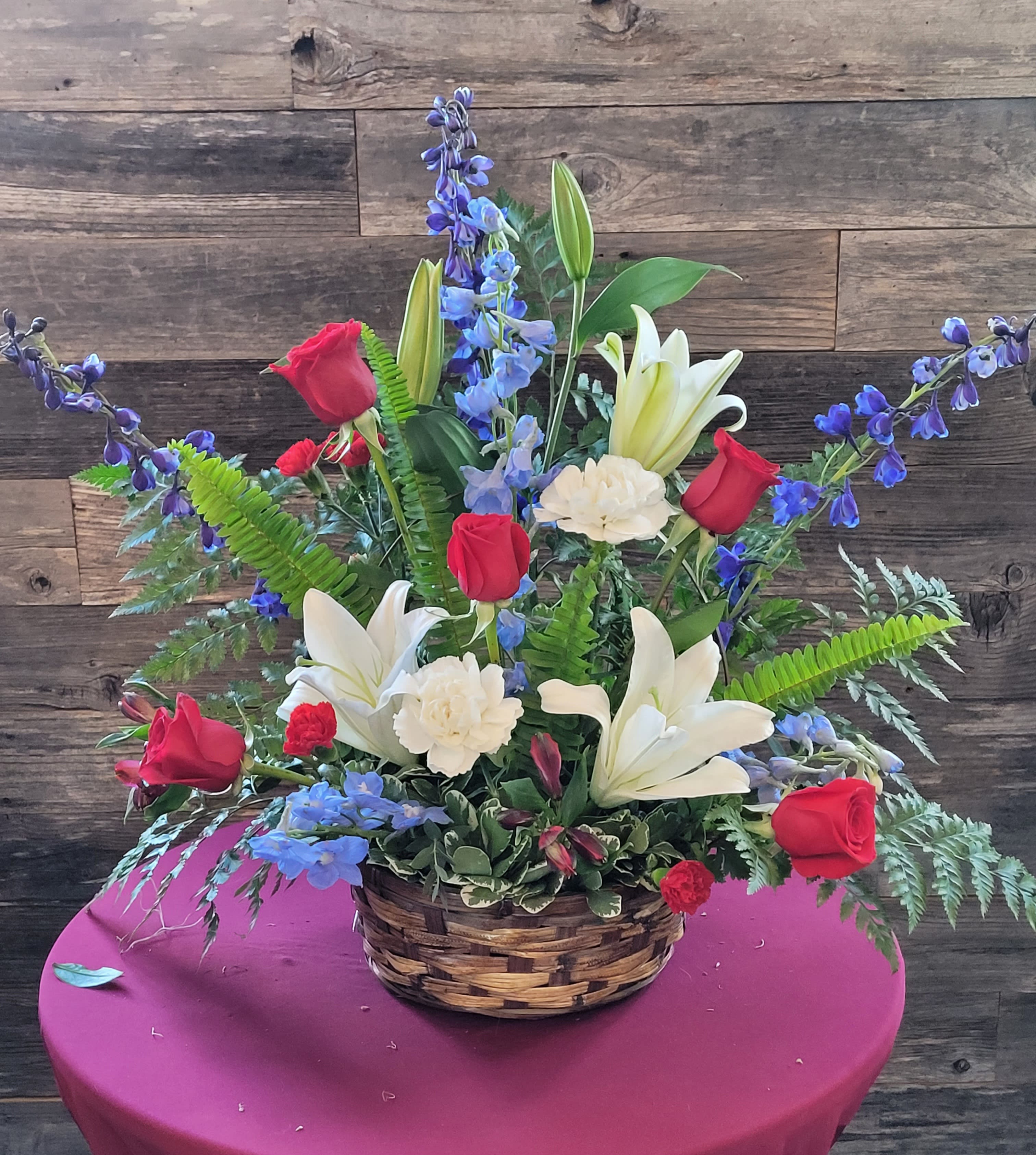 Basket arrangement with red roses, white lilies, and blue flowers