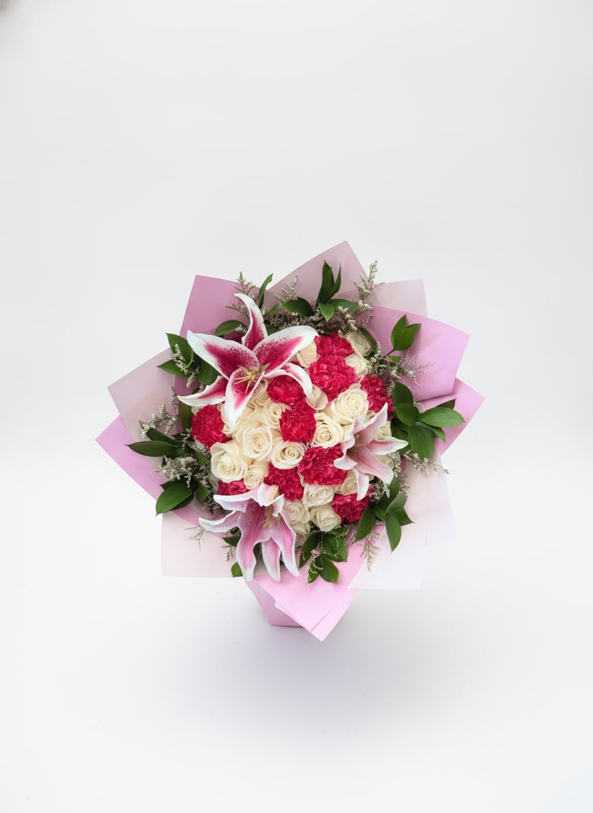 Sweet Devotion - Cream roses and pink-and-white lilies mingle with bright pink carnations in a rounded hand-tied flower arrangement that reads both romantic and joyful-perfect as a birthday bouquet, anniversary roses alternative, or a just-because gift to show affection. The soft cream of the roses balances the vivid pink clusters for a feminine, celebratory look that will make the person you're thinking of feel cherished and seen.  This arrangement features lilies, roses, and carnations with glossy green foliage and delicate filler for texture, all wrapped in layered pink paper for a polished presentation. The compact, rounded design is hand-tied for a natural, easy-to-hold shape; colors are cream, pink, white, and green which work well across springtime, Valentine's Day, or Mother's Day gifting. Order for same-day delivery when available to ensure the lilies arrive fresh and fragrant.