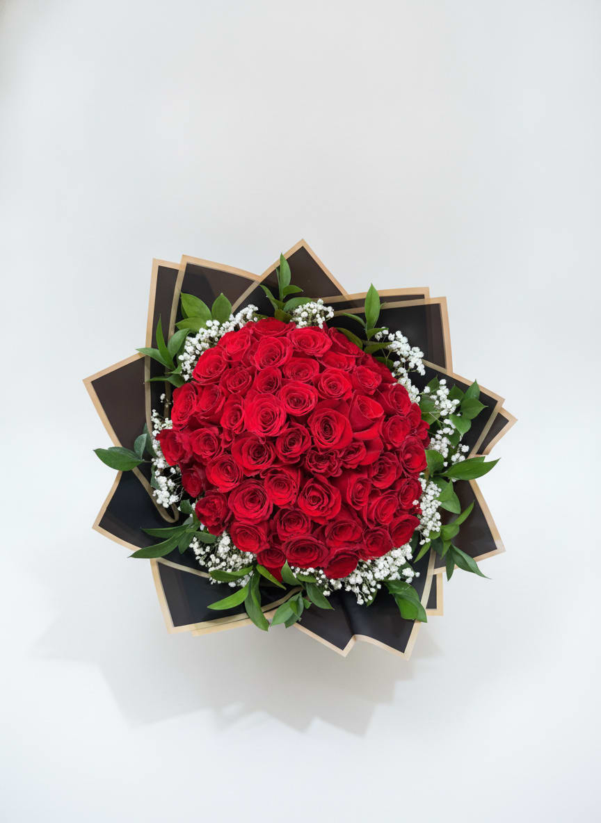 Eternal Romance - A dense, rounded cluster of deep red roses creates an immediate statement-perfect as an anniversary bouquet or a love-and-romance gift that feels dramatic without being fussy. The Ramo Buchon reads as intent: the rich crimson heads draw the eye while small white filler blooms and bright green foliage soften the silhouette so the person you're thinking of will feel deeply noticed and adored.  Wrapped in layered black paper with kraft (tan) edging, the presentation is modern and bold, the dark wrap amplifying the roses' color and giving the arrangement a polished, gift-ready look. Medium-to-large in scale and styled for hand delivery, the bouquet combines classic rose stems, delicate white accents, and fresh greenery for a tactile, fragrant bouquet that photographs beautifully and holds at-home presence.  Ideal for anniversaries, birthdays, Valentine's Day, or simply to say "I'm sorry," "thinking of you," or "just because," this bouquet reads romantic and sincere across occasions. To keep it looking its best, place in fresh water on arrival and recut stems if needed-its full, rounded shape makes an immediate impression the moment it's handed over.