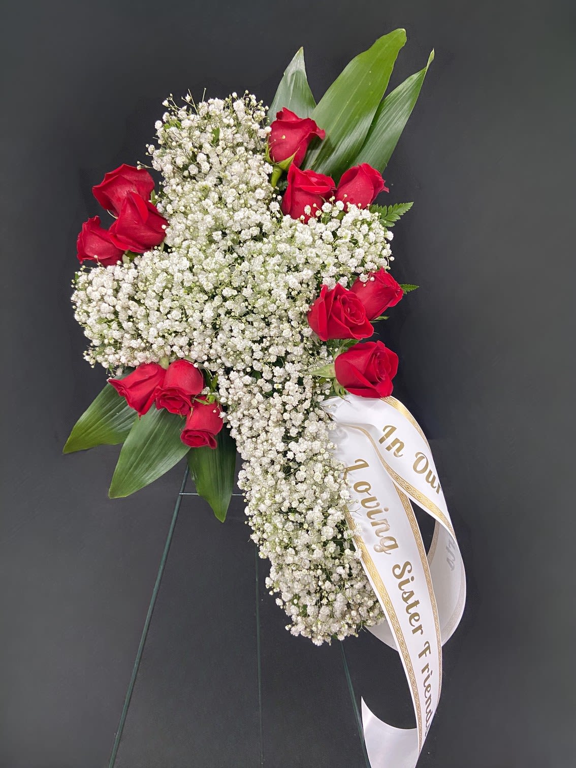 Baby's Breath Cross Standing Spray - An elegant cross of white baby's breath accented with roses of your color choice and tropical aspidistra leaves mounted on a standing easel.