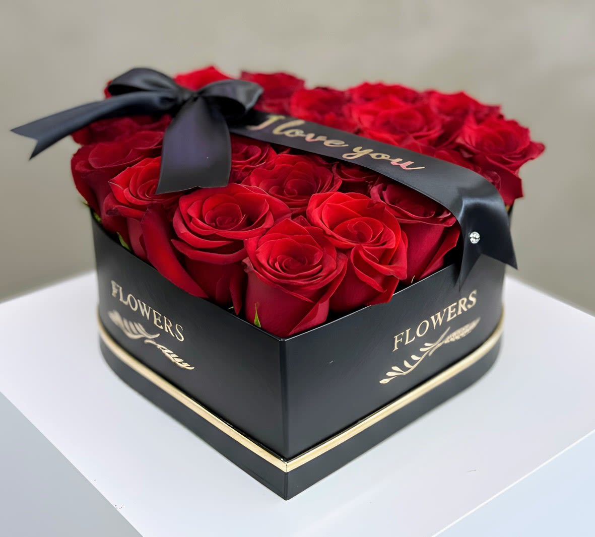 Red roses arranged in a black heart-shaped box with a ribbon