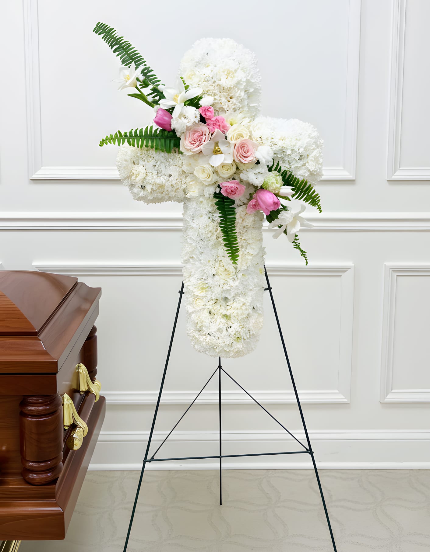 White funeral spray with pink roses and lilies on a stand beside a casket