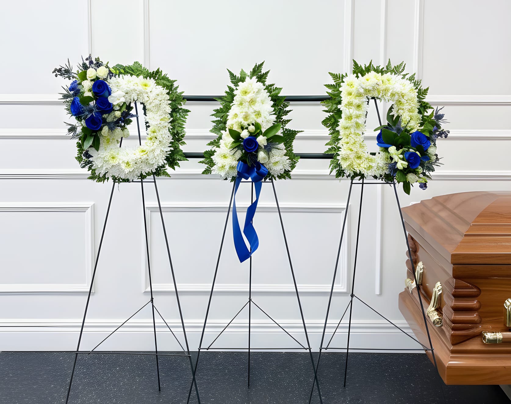 Three funeral wreaths on stands beside a casket