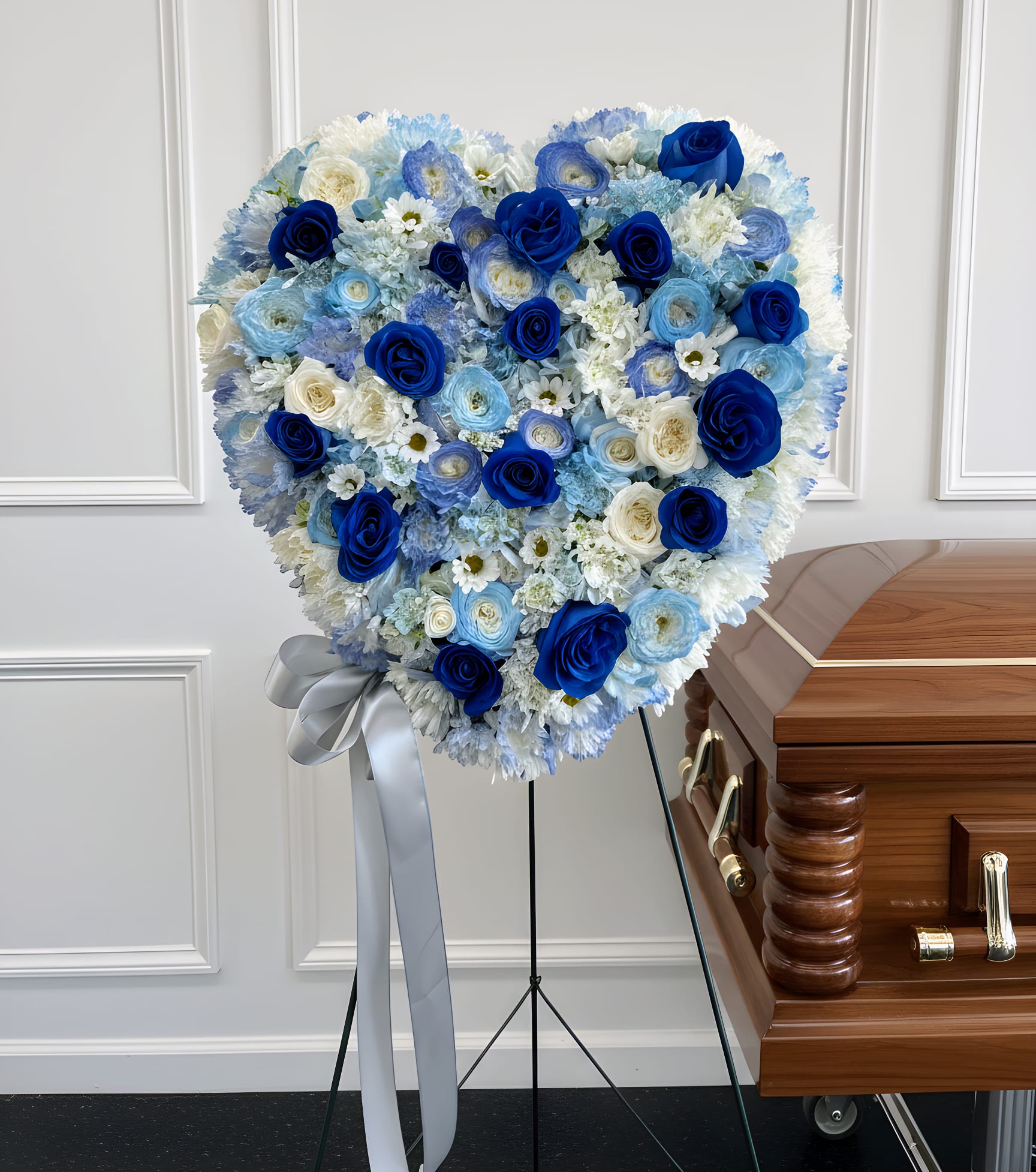 Heart-shaped blue and white floral funeral spray beside a casket
