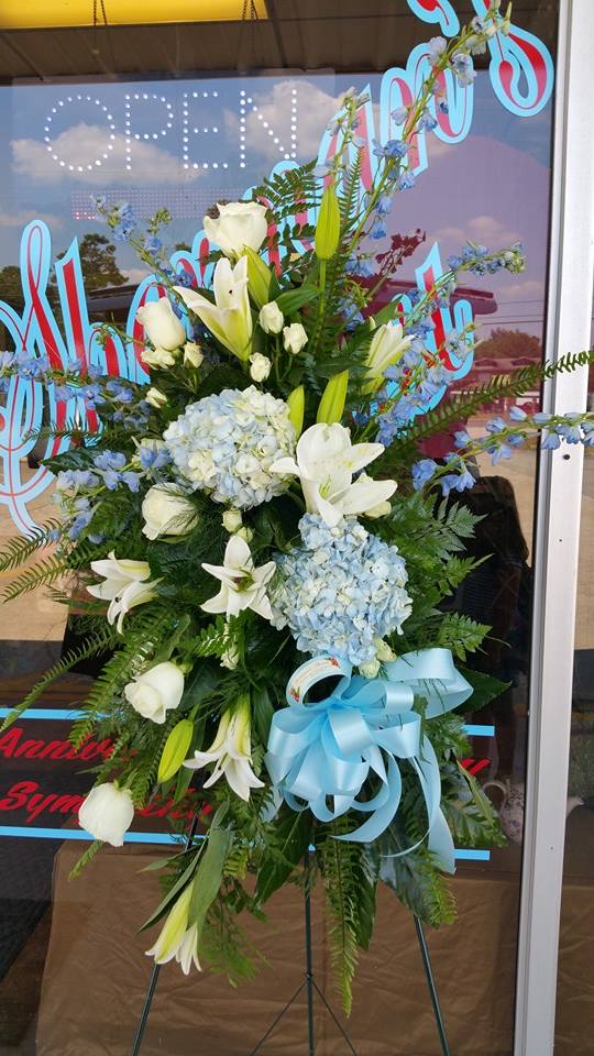Standing floral spray with white lilies, blue hydrangeas, and a blue ribbon