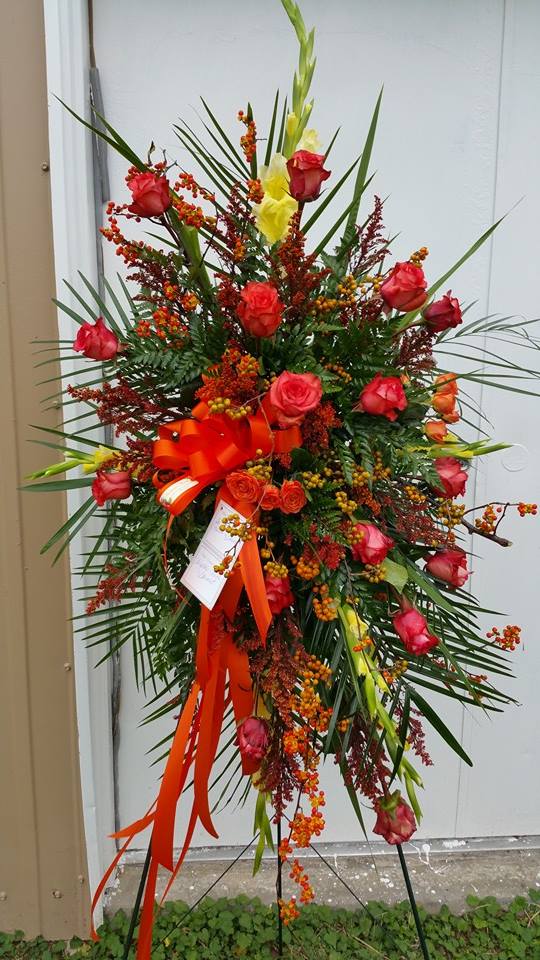 Tall standing floral spray with red roses and orange berries on an easel