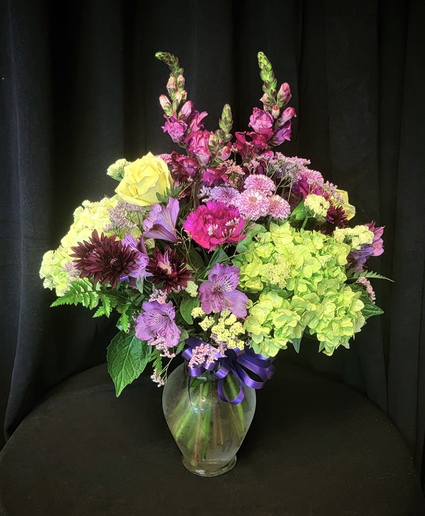 Mixed bouquet of purple, pink, and yellow flowers in a glass vase