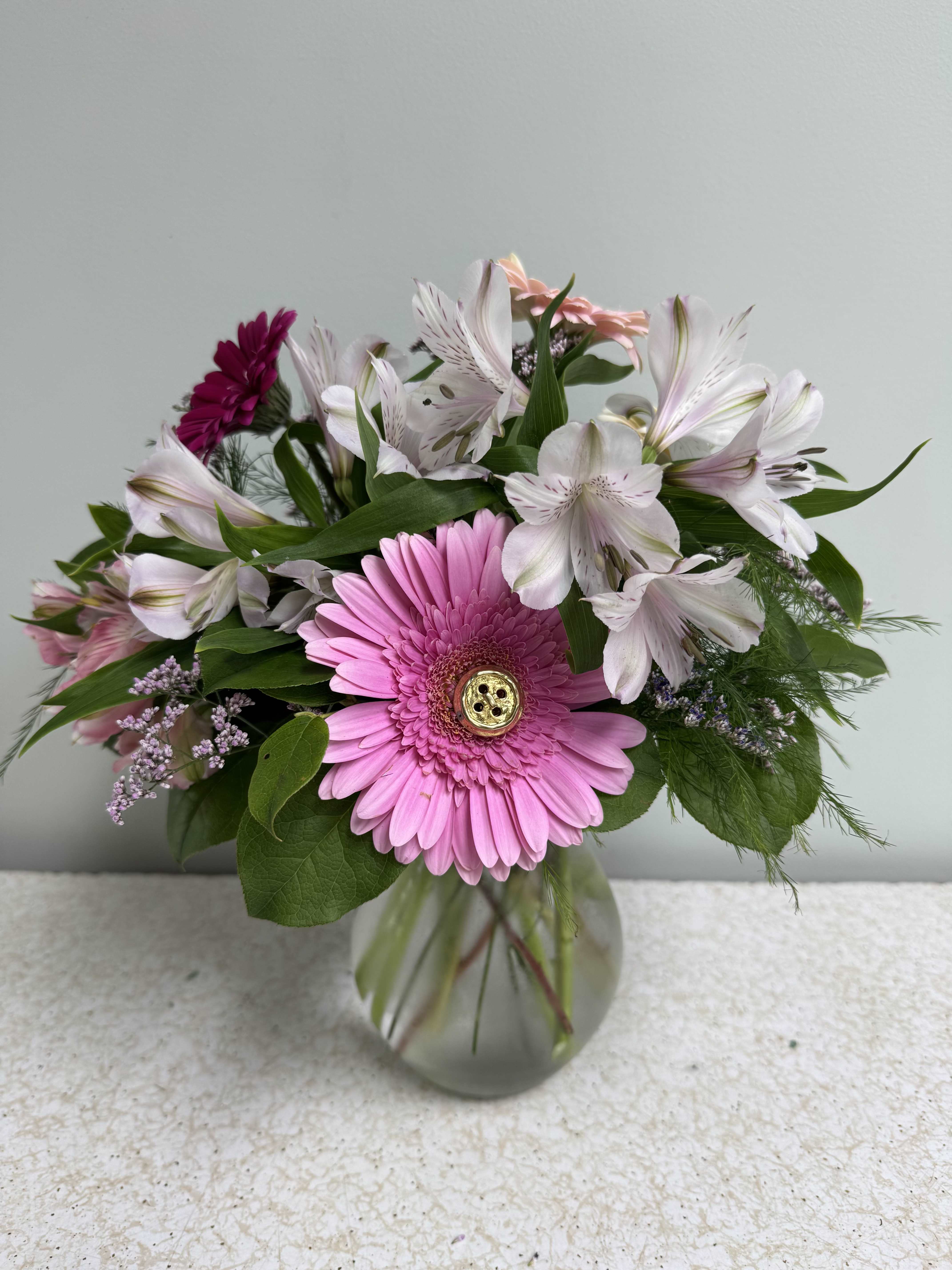 Cute as a Button - This little arrangement has 3 large gerbera daisies and 2 mini gerbera daisies, 4 stems of alstromerium, and filler. But here's the best part: two of the gerberas have cute little buttons attached to the centers! It's so cute we CAN'T TAKE IT.  You can ask for a certain color palette under special instructions. 
