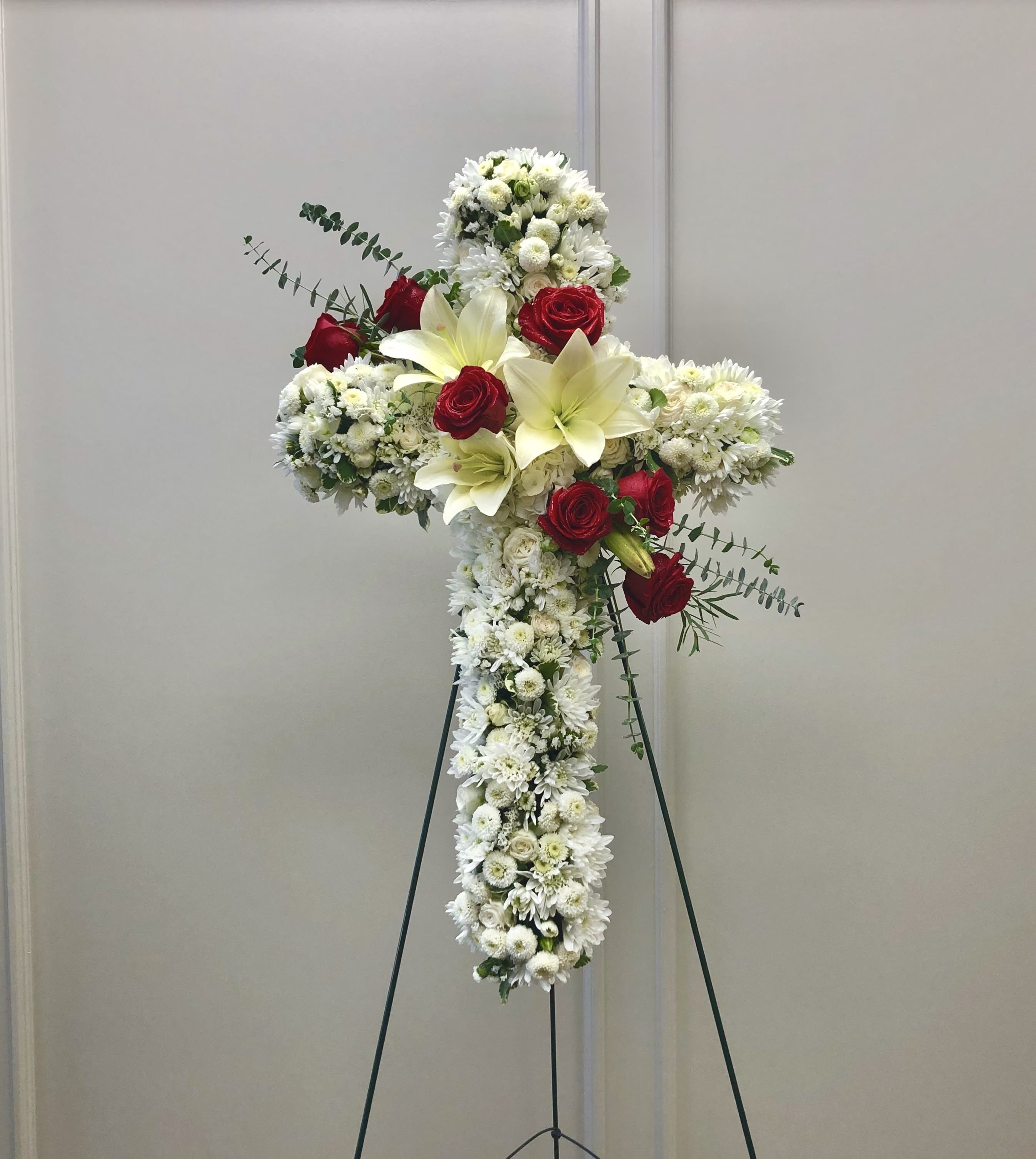White floral cross on a stand with red roses and lilies
