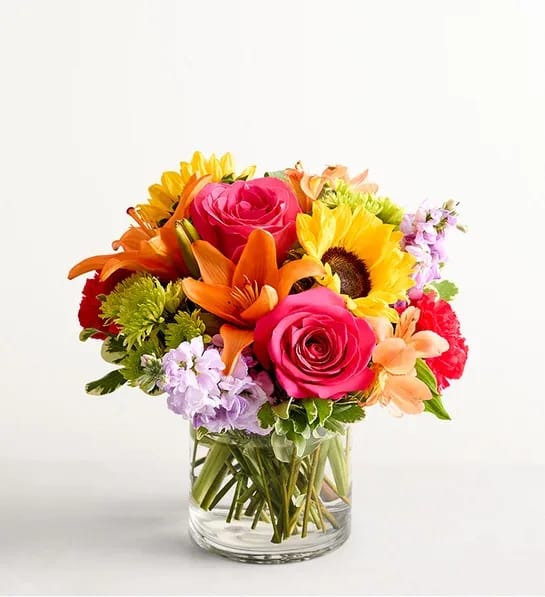 Colorful bouquet of roses, lilies, and sunflowers in a clear glass vase