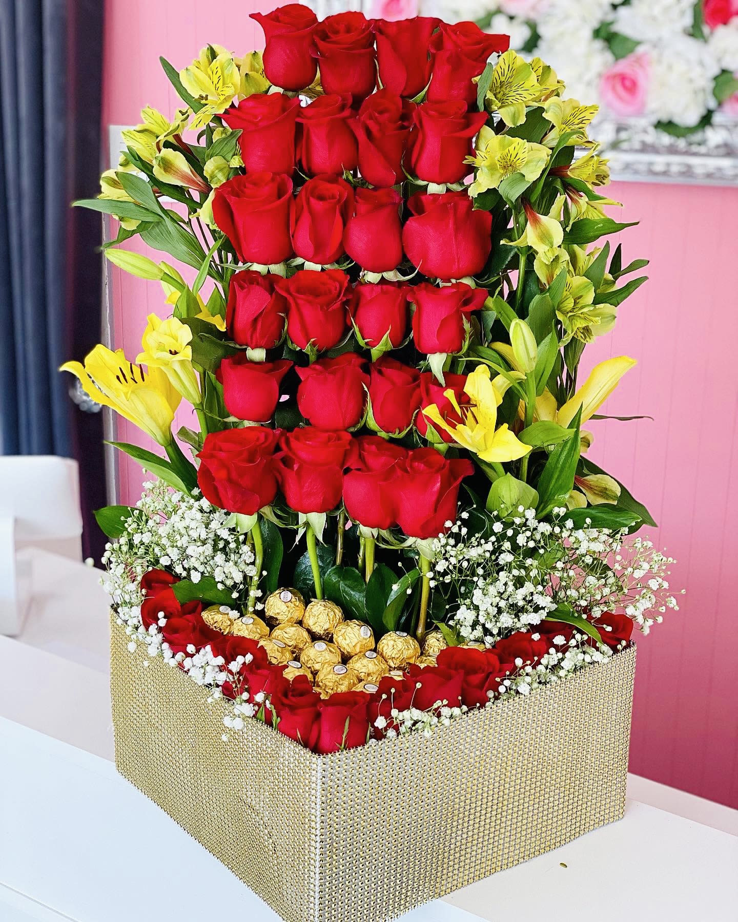 Tall box arrangement of red roses with yellow lilies and gold chocolates