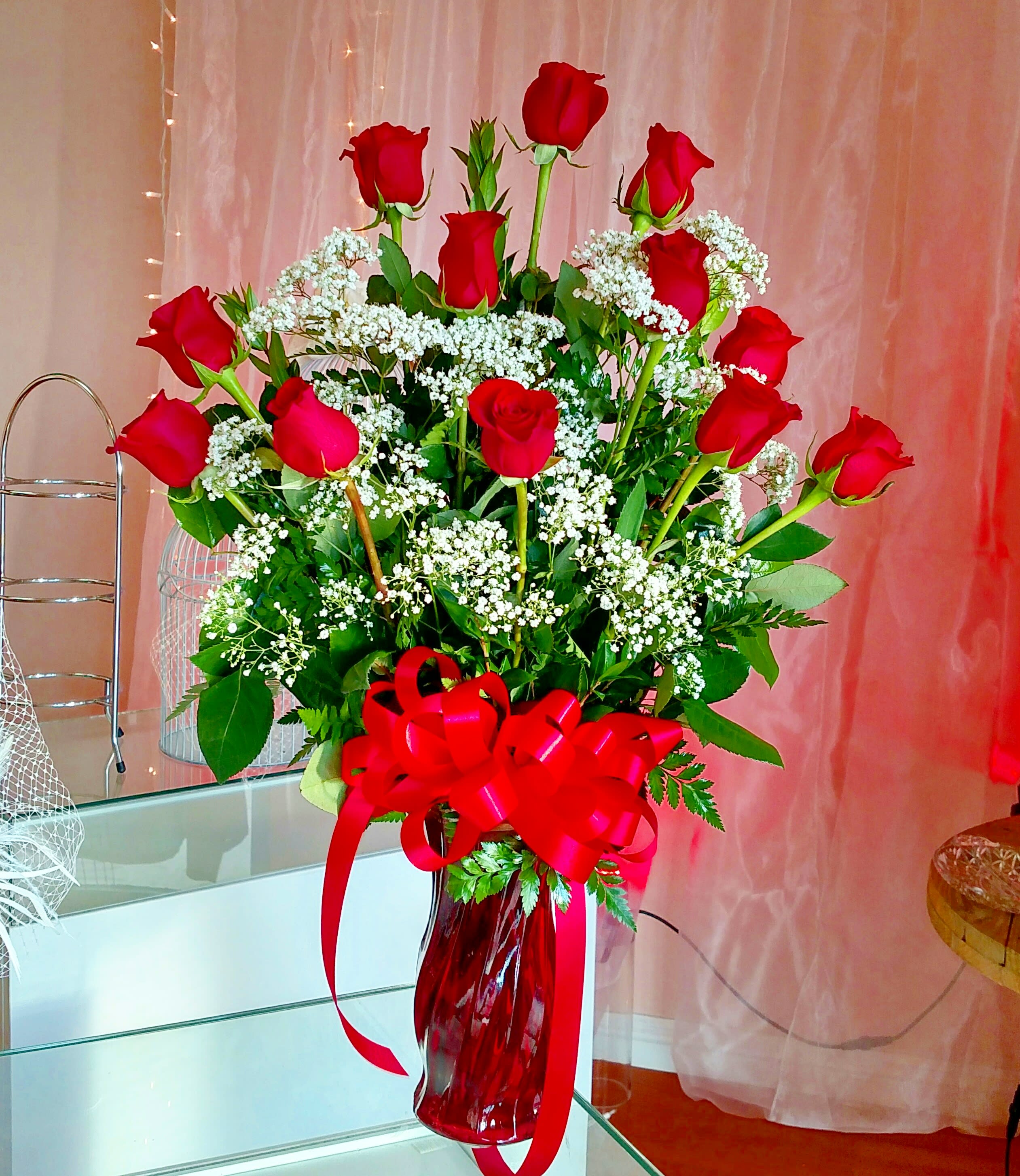 Red roses arranged in a red glass vase with a large ribbon bow