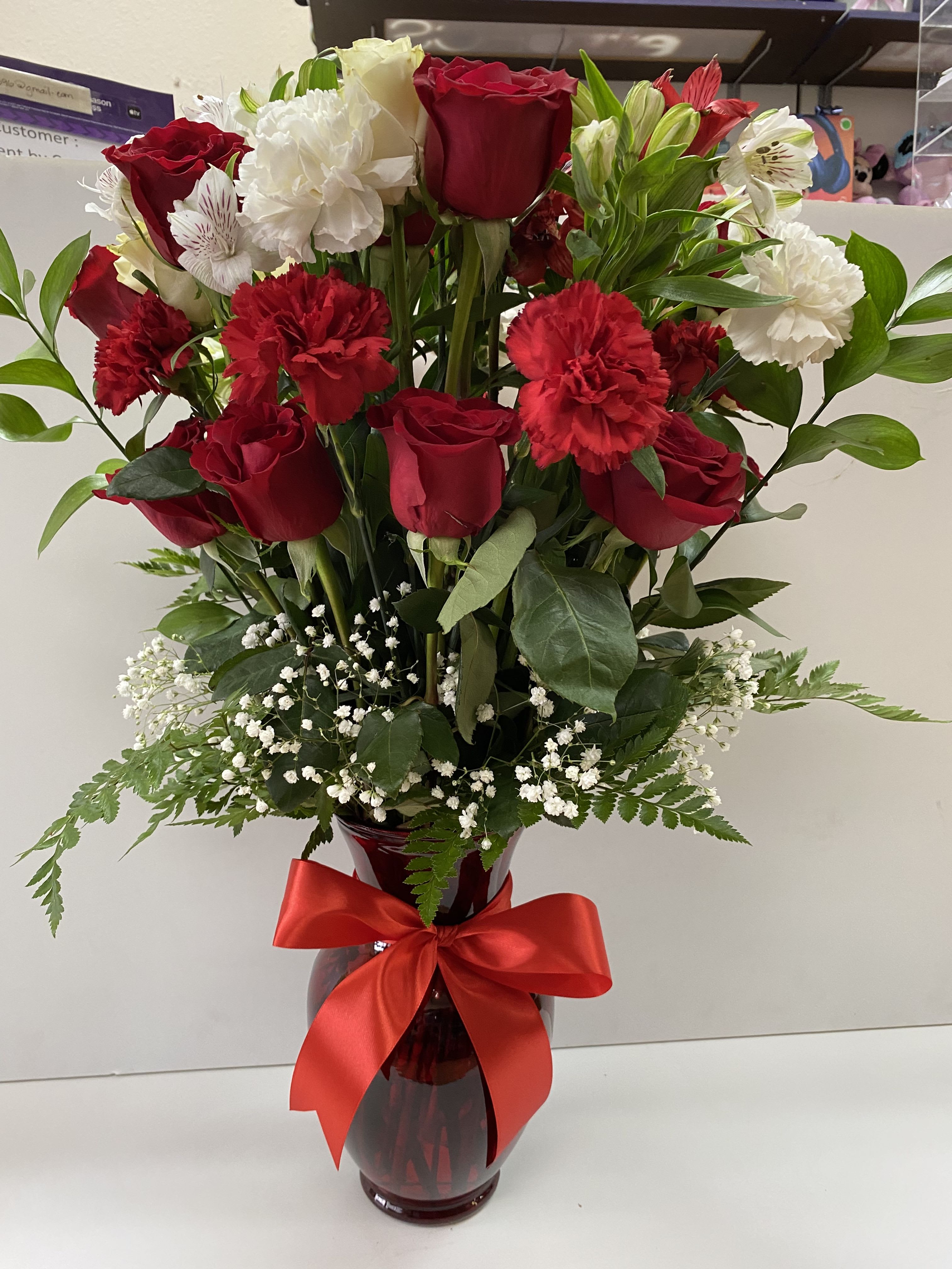 Tall arrangement of red roses and carnations with white blooms in a red vase with a red bow