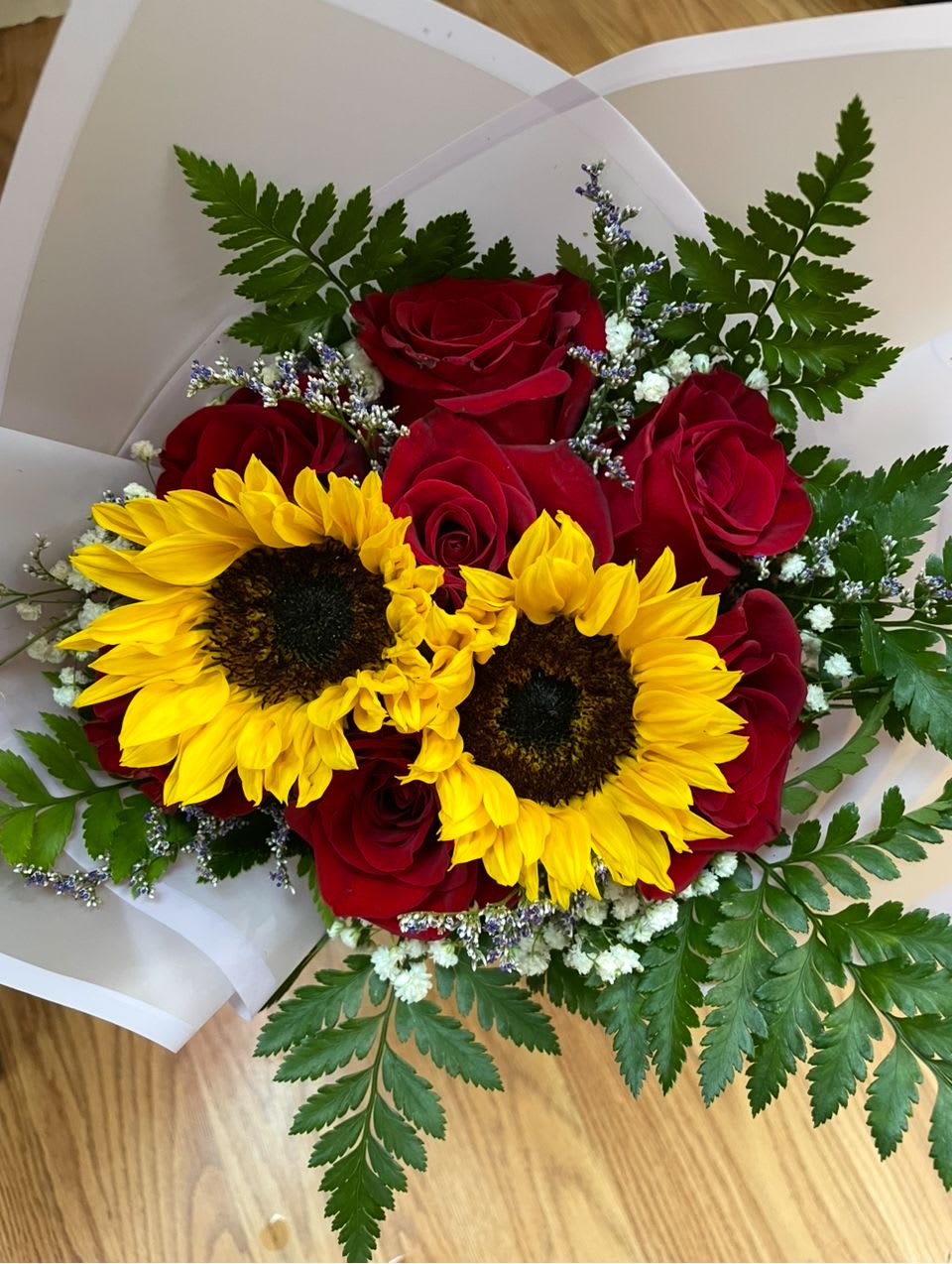 Bouquet of red roses and yellow sunflowers wrapped in white paper