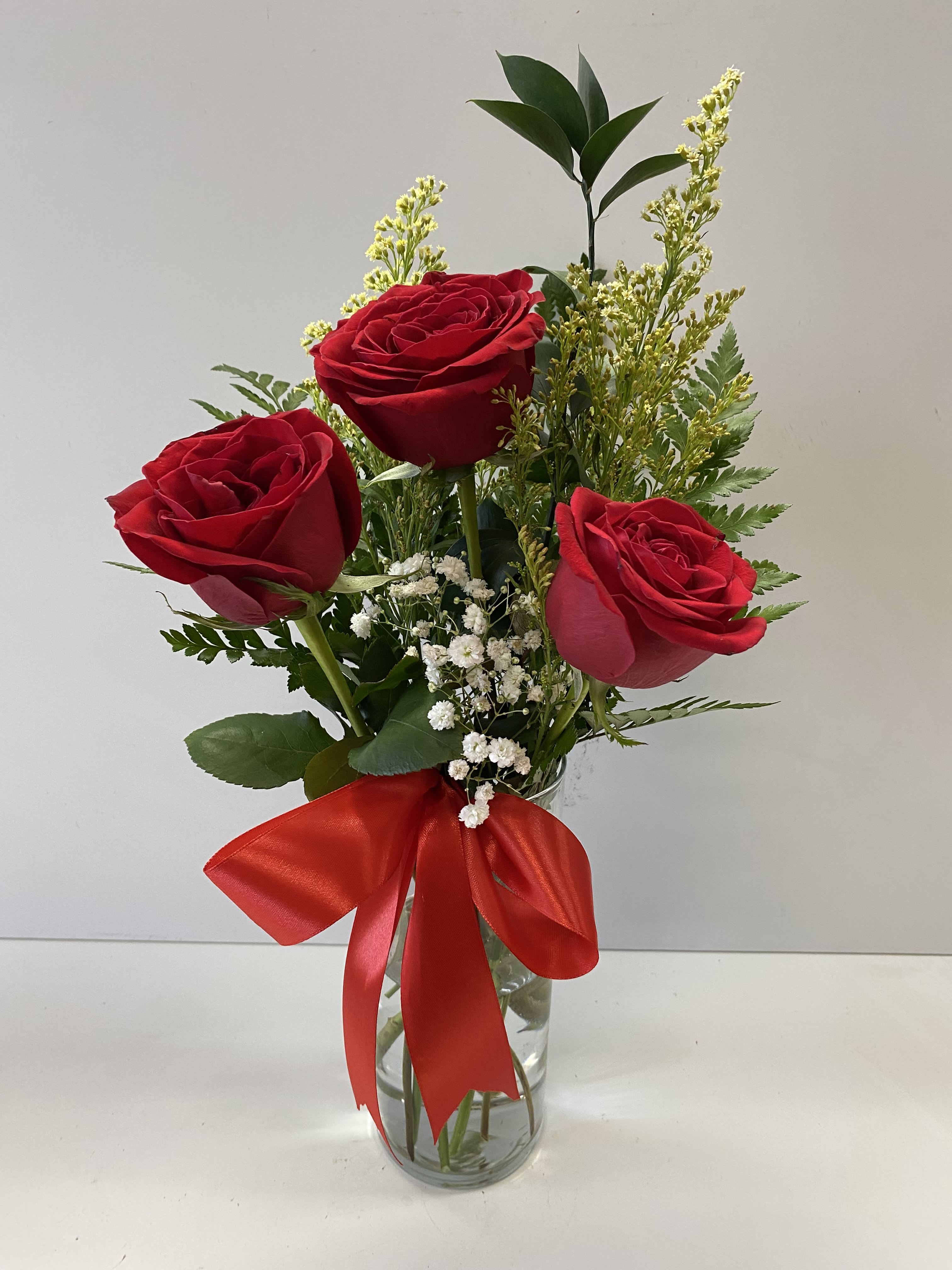 Three red roses in a clear glass vase with a red ribbon