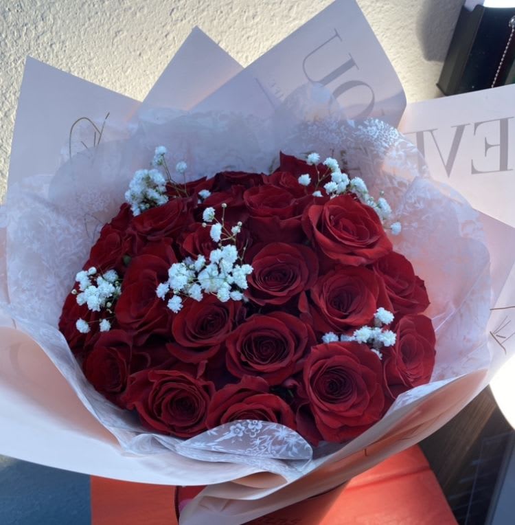 Hand-tied bouquet of red roses with white filler flowers wrapped in soft pink paper