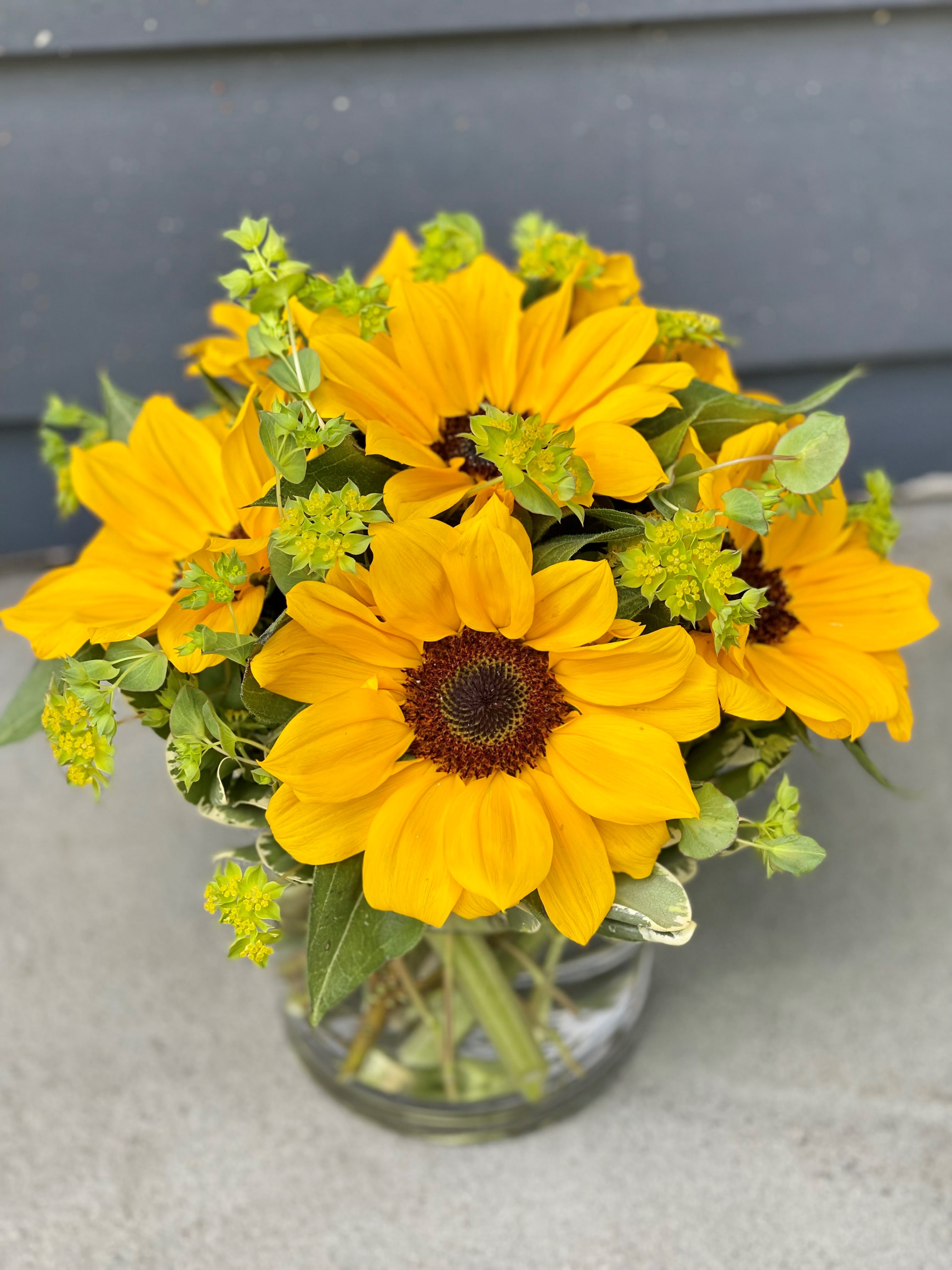 Sunny Sunflowers - Nothing says "Summer" better than a vase full of sunny sunflowers. Always cheerful and happy, sunflowers accented with subtle greenery in a clear glass cylinder.