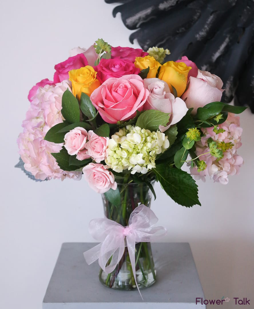 Bouquet of pink, yellow, and white roses in a glass vase with a ribbon