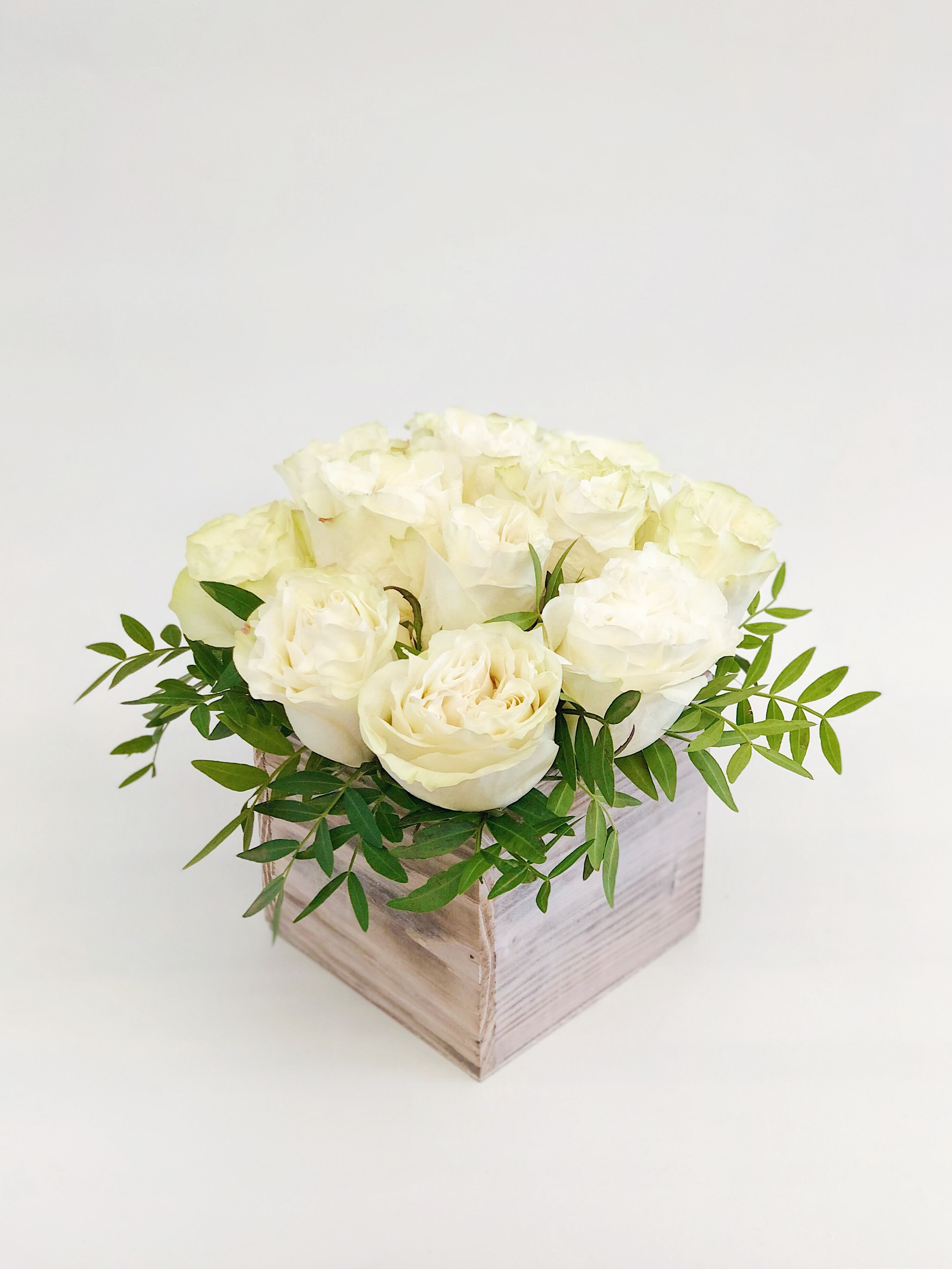White roses arranged in a square wooden box with green foliage