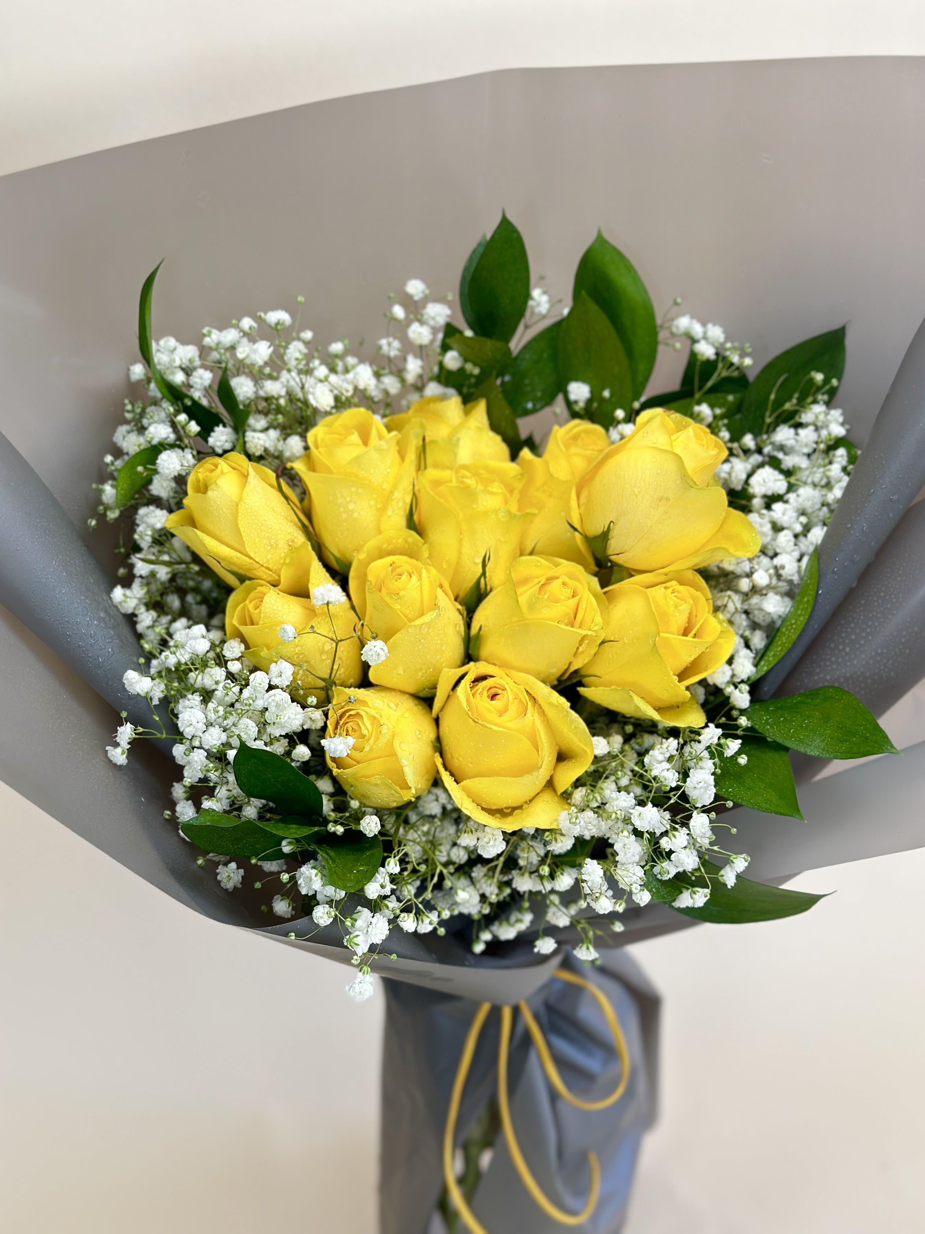 Bouquet of yellow roses with white baby's breath in gray wrapping