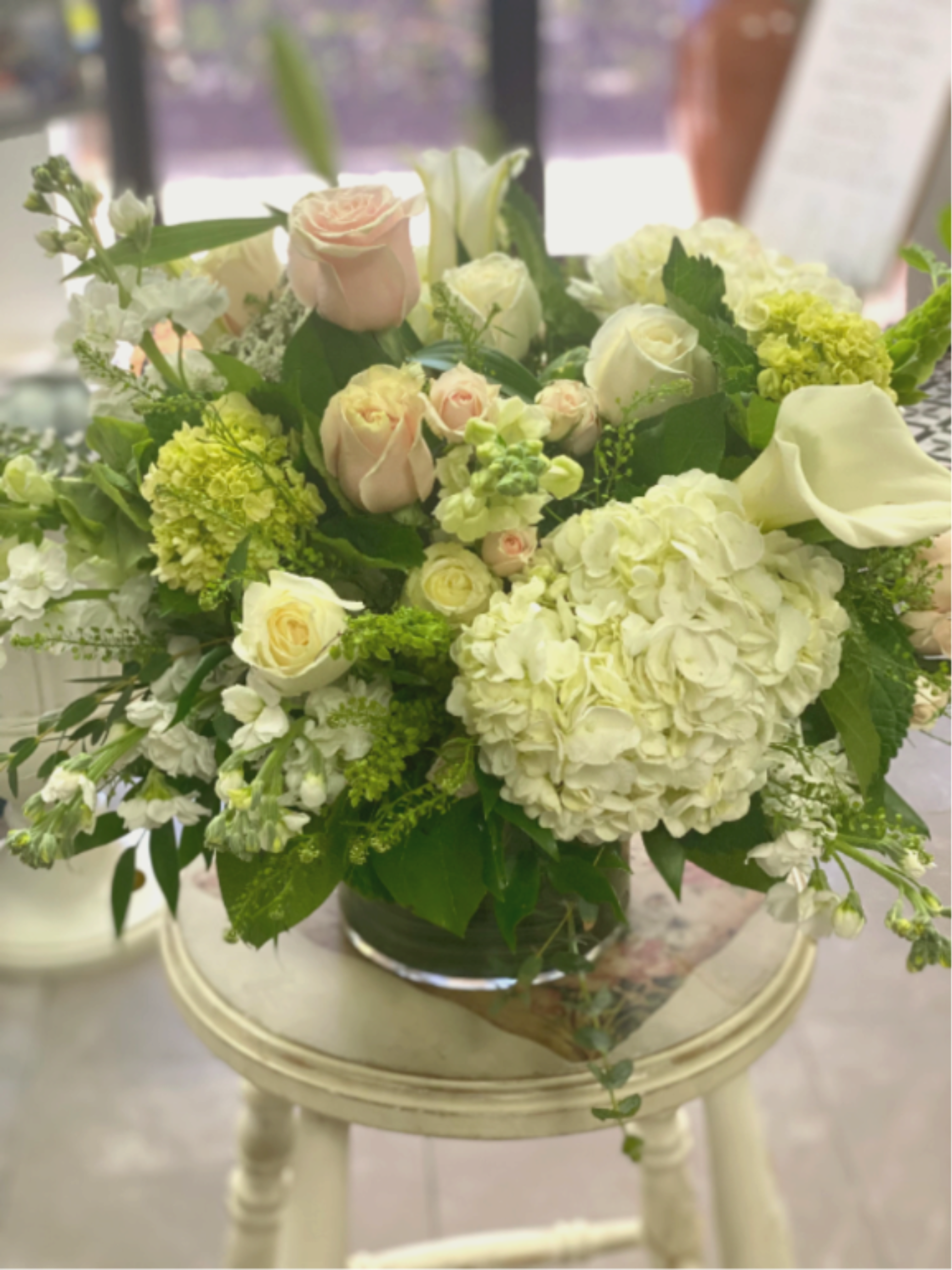 Mixed bouquet of pale roses, hydrangeas, and white calla lilies in a glass vase