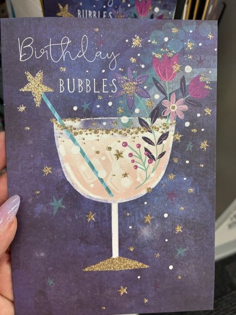 Birthday Bubbles Card - A playful birthday card that reads like a mini celebration: the Birthday Bubbles Card features a deep purple background and a whimsical champagne coupe illustration filled with sparkling bubbles, small stylized flowers, stars, and gold accents. Designed for birthdays but perfectly suited for love and romance, just-because notes, or congratulations, this cheerful card sends a lighthearted, celebratory message that will make the recipient feel special and noticed.  Printed in a palette of pink, white, teal, and gold against the dark backdrop, the design feels both festive and slightly elegant-ideal for slipping into a bouquet, tucking with a small gift, or sending solo with a handwritten note. Each card includes a coordinating blank interior so you can write a personal message; pair it with bright yellow, white, purple, or pink flowers to echo the colors and amplify the joyful, bubbly mood.