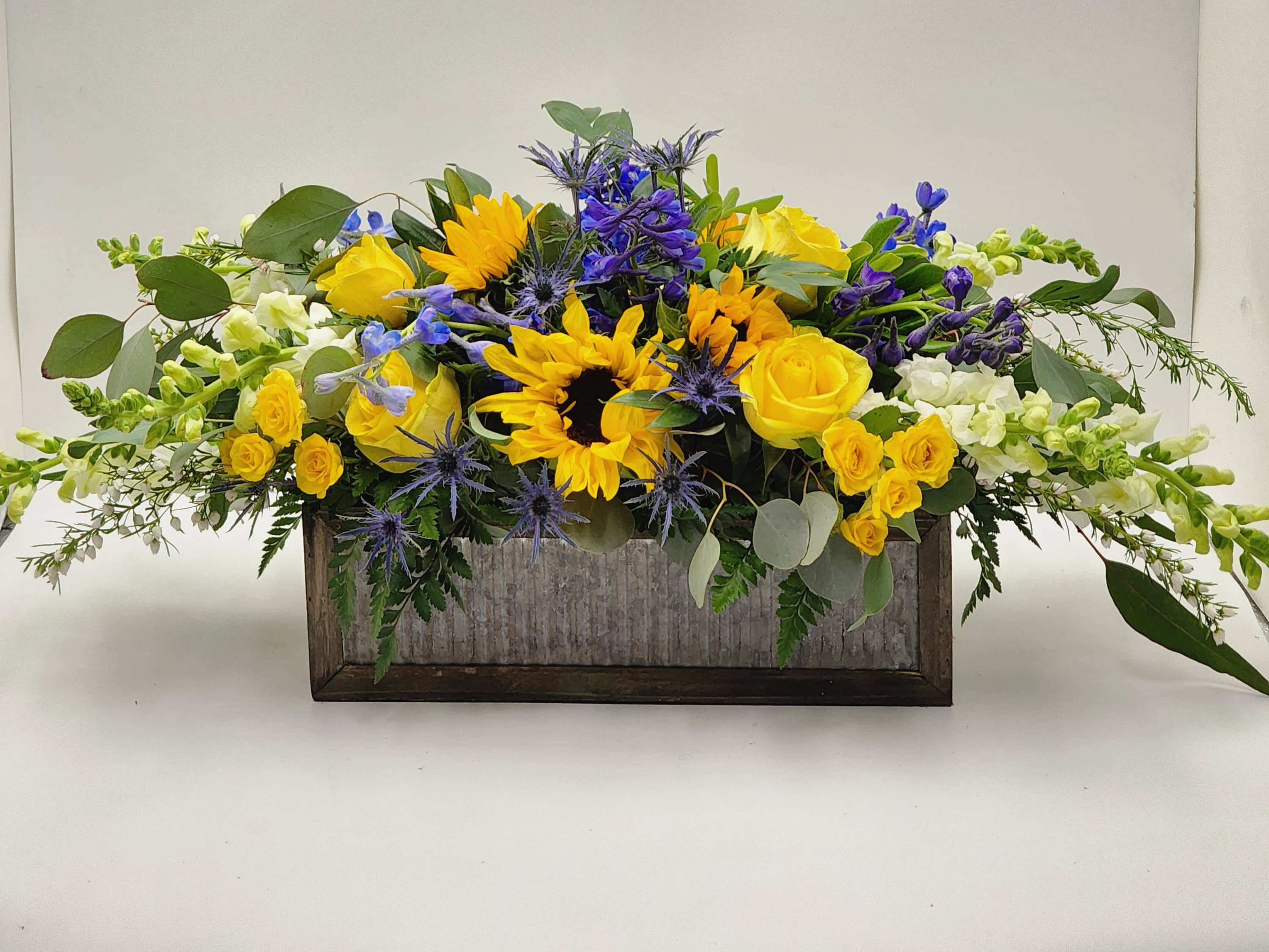 Garden of Sunshine - A wooden box filled with blue and yellow flowers including roses, sunflowers, snapdragons, spray roses and belladonna.  Roughly 32x13x14