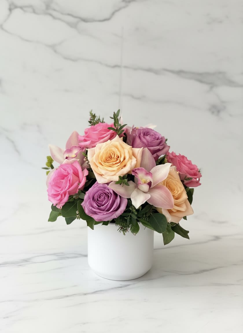 Spring on Polk Street - Rounded clusters of pastel roses and orchids create an immediately cheerful, romantic impression-perfect as an anniversary bouquet, birthday surprise, or a bright "just because" gift. This flower arrangement reads like spring on Polk Street: soft pinks, peaches, lavenders and a touch of purple combine to make the recipient feel truly celebrated, whether you're saying thank you, welcome to the new baby, or marking a milestone.  Nine roses in bright pink, peach and lavender are packed into a compact, dome-shaped design and accented with a few pale cymbidium orchid blooms and small sprigs of greenery. The composition sits in a clean white ceramic vase that keeps the focus on the soft, mixed-color palette and gives a modern, keepsake feel. Sized for tabletops and desks, it's a polished, pet-friendly choice for Mother's Day, Valentine's Day, Admin Professionals' Week, or any congratulatory moment-simple care: fresh water and a cool spot help the blooms last longer.