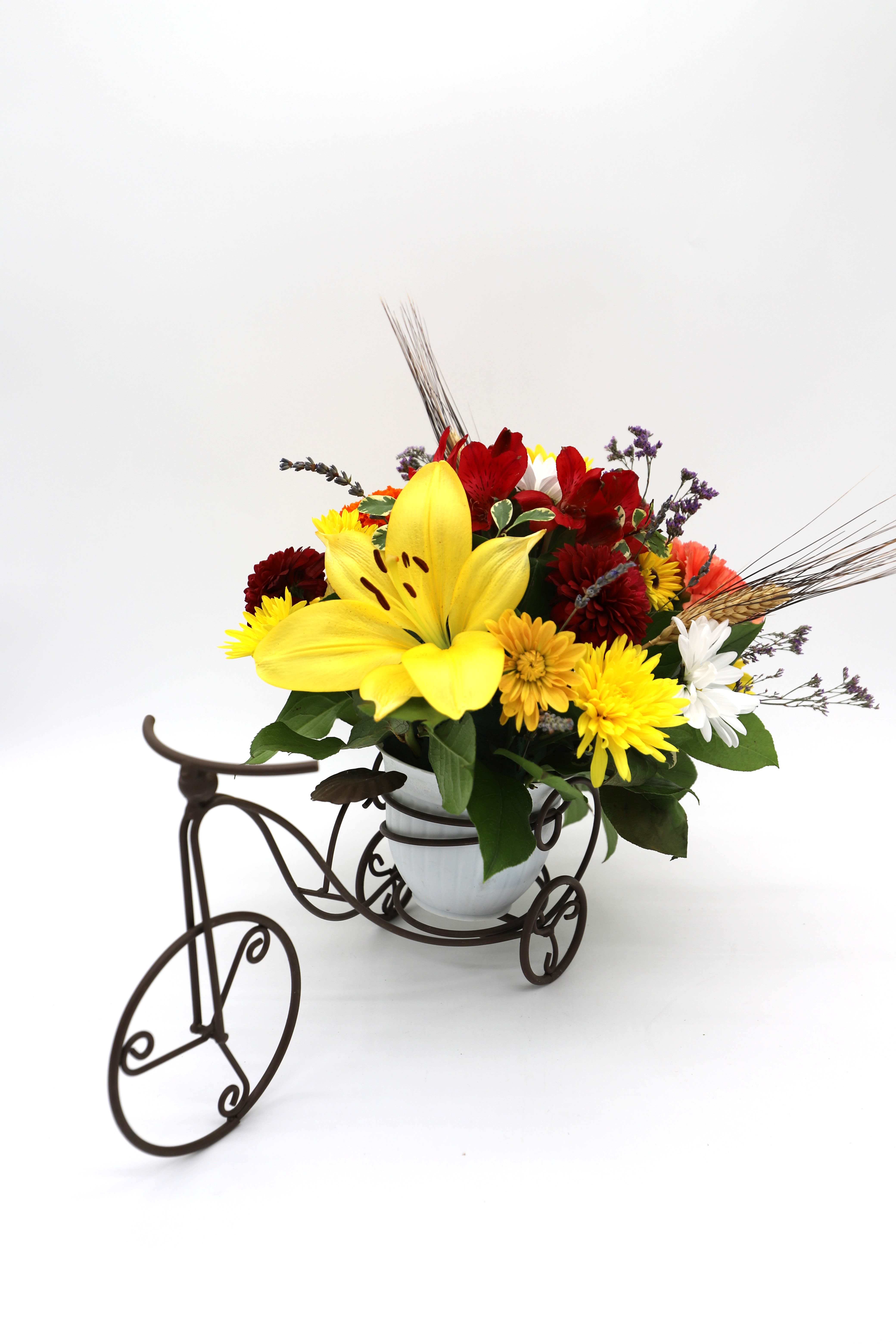 Mixed bouquet with a large yellow lily in a white vase on a decorative tricycle stand