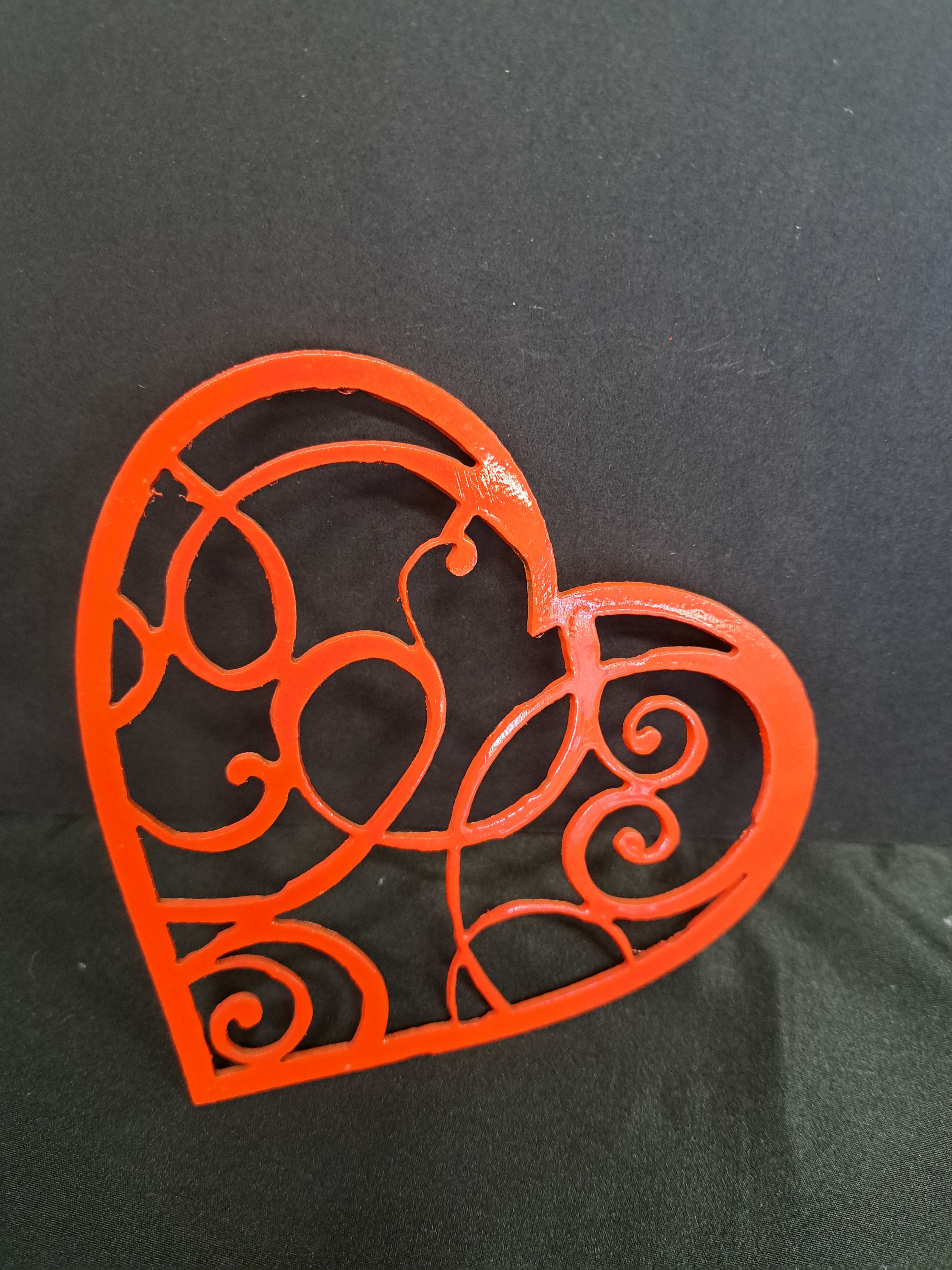 Metal Heart wall hanger Scroll pattern - Crafted as a rigid, heart-shaped metal cutout with intricate scrollwork, the piece is finished in vivid red (or a brushed silver alternative shown) that contrasts beautifully against dark backgrounds for maximum visual impact. The openwork design creates texture and shadow play on the wall; no floral components are included. Sized to work as a standalone accent, it pairs easily with existing wall groupings or above a mantel for a clean, contemporary look.