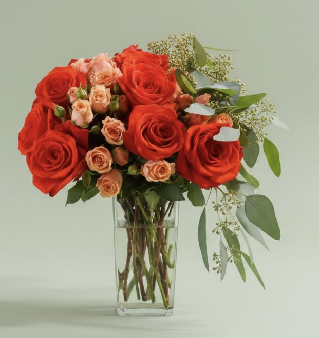 Vibrant Roses Mix - A bold cluster of vivid red roses softened by peach spray roses creates an effortless romantic statement-perfect as an anniversary bouquet or a surprise for love and romance. This flower arrangement reads both classic and lively, making the recipient feel cherished whether you're marking a birthday, saying thank you, or sending a "thinking of you" moment.  Arranged in a tall clear glass vase, the Vibrant Roses Mix pairs dense red roses with smaller peach-toned spray roses for warm contrast, while airy eucalyptus and fine filler extend to one side for a loose, asymmetrical silhouette. The glass vase lets stems show through for a clean, contemporary look; colors include rich red, gentle peach, touches of pink and green foliage for a mixed-color effect that suits spring and summer occasions without feeling seasonal.  For weddings, Mother's Day, Valentine's Day, or a simple "just because," this arrangement reads as heartfelt and celebratory-the kind that makes someone feel truly seen. Arrives ready-to-display in its vase; trim stems and refresh water with floral preservative every 2-3 days to keep blooms vibrant.