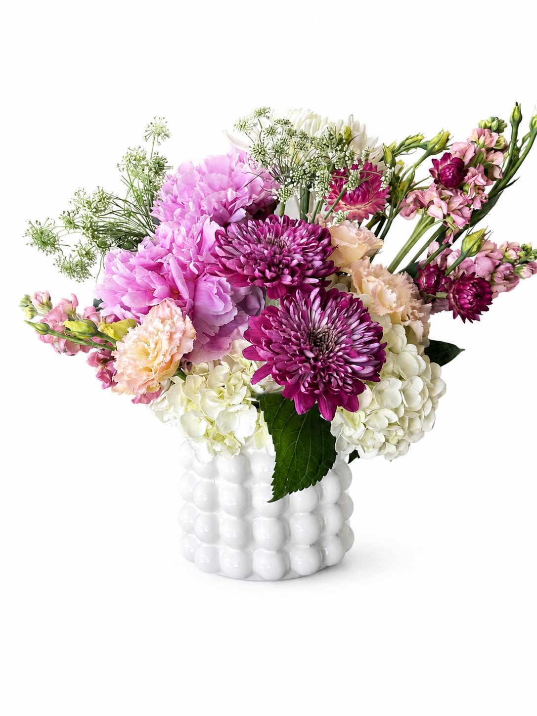 Pink Velvet - Big, fluffy pink and white hydrangea clusters steal the show in this floral arrangement, making it the perfect birthday bouquet or cheerful thank-you gift that reads fresh and feminine. Designed as an everyday celebration piece, Pink Velvet pairs vivid magenta chrysanthemums and soft peach carnations so the person you're thinking of will feel noticed and adored the moment they see it.  The mix also includes delicate, airy filler flowers for a garden-like texture against a modern white ceramic vase with rounded, bubble-like detailing-clean, decorative, and keeps the focus on the blooms. Colors span pink, white, purple-magenta, and peach for lively contrast; the hydrangeas provide volume, chrysanthemums add punchy color, and carnations bring soft, lasting charm.  Send this arrangement to brighten a spring celebration, say thanks, or mark a casual milestone-the kind of bouquet that makes someone feel genuinely celebrated. Vase included; arrange in a cool spot away from direct sun to extend bloom life and refresh the water every other day.