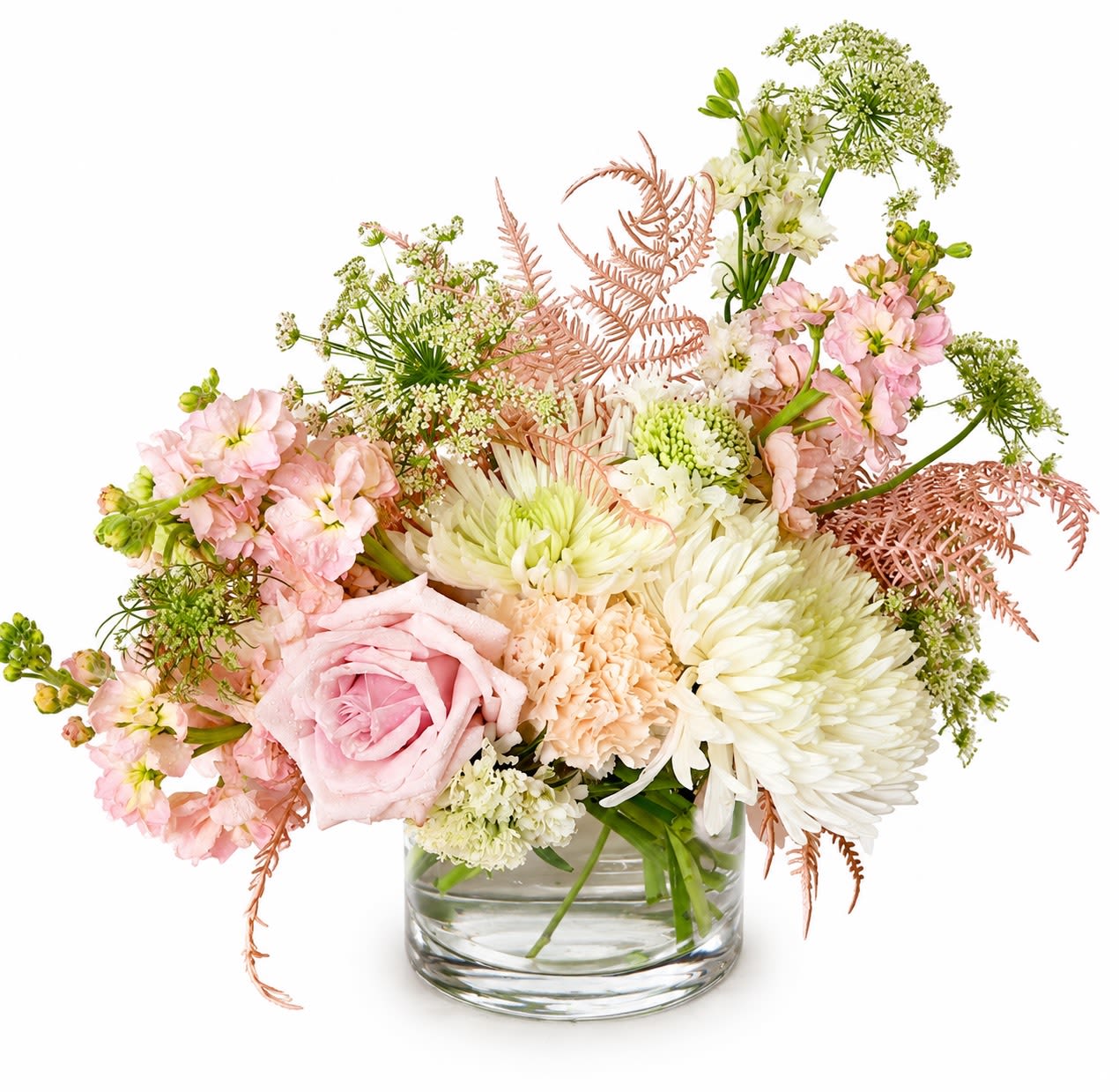 Boho Daydream - Soft pink roses and pale peach carnations mingle with white chrysanthemums and airy white stock in a garden-style birthday bouquet that feels like a gentle, romantic sigh. The Boho Daydream is a spring-ready arrangement perfect for birthdays, Mother's Day, anniversaries, or any moment you want the person you're thinking of to feel softly celebrated.  Arranged loose and full in a clear glass vase, the design uses delicate branching accents and light green foliage to create a relaxed, bohemian silhouette-soft pastels and varied textures that read both elegant and effortlessly casual. Sized to sit on a mantel or bedside table, it arrives ready to display; simple care-fresh water and a clean vase-keeps the blooms happy for days.