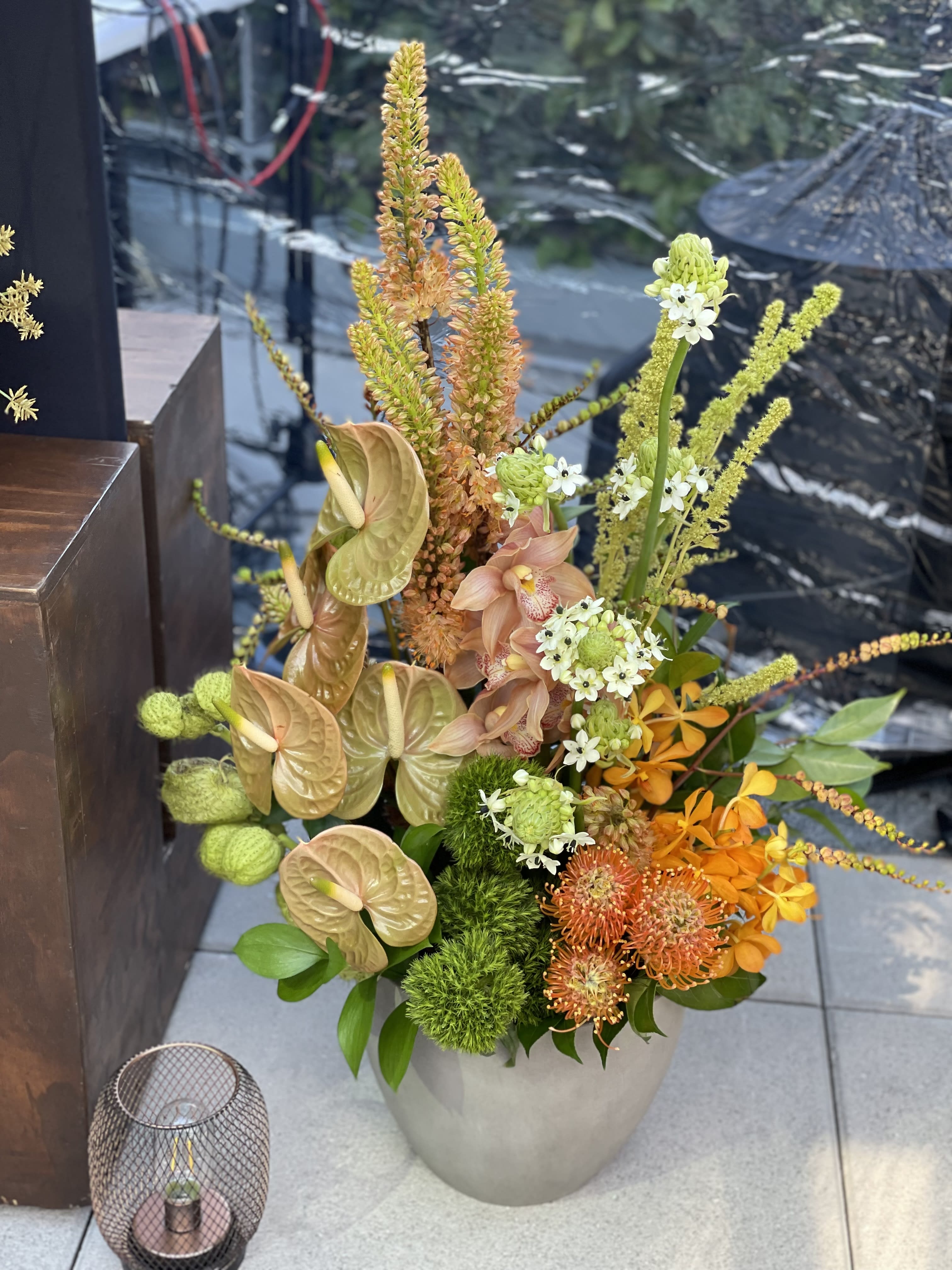 Tall mixed floral arrangement in a gray vase with orange, green, and peach blooms