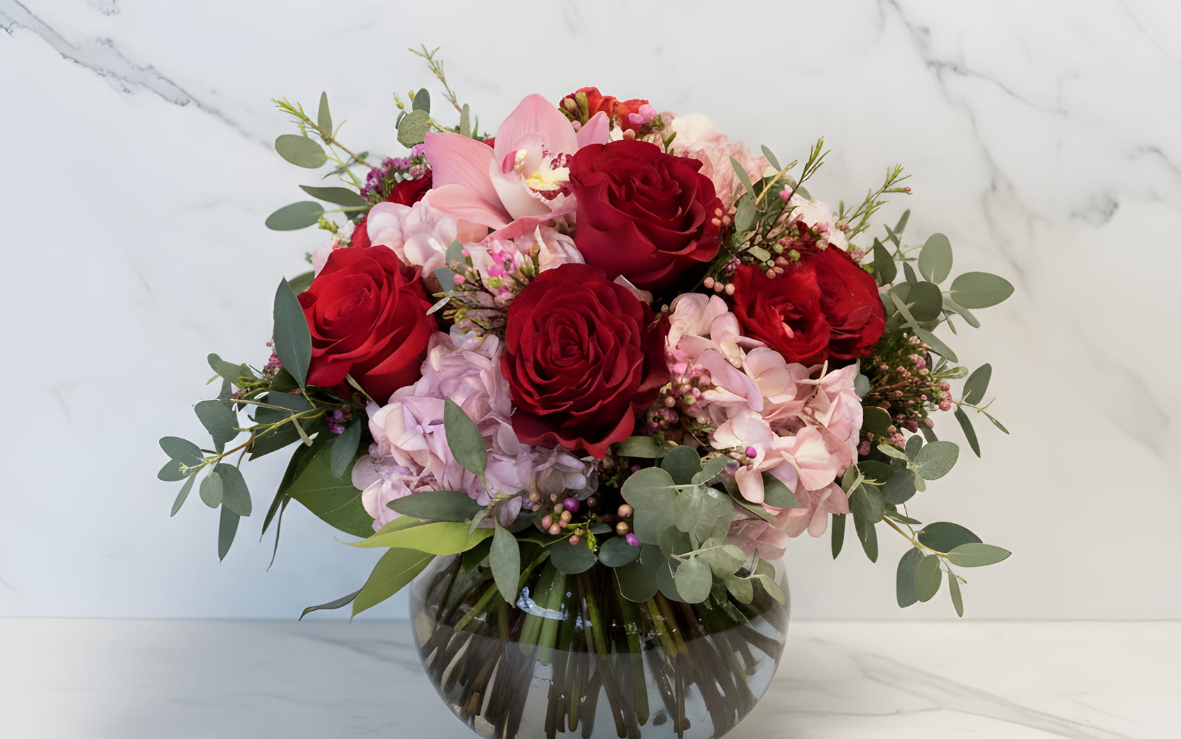 Bouquet of red roses and pink orchids in a glass vase