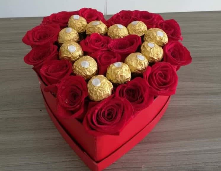 Heart-shaped box of red roses topped with gold-wrapped chocolates