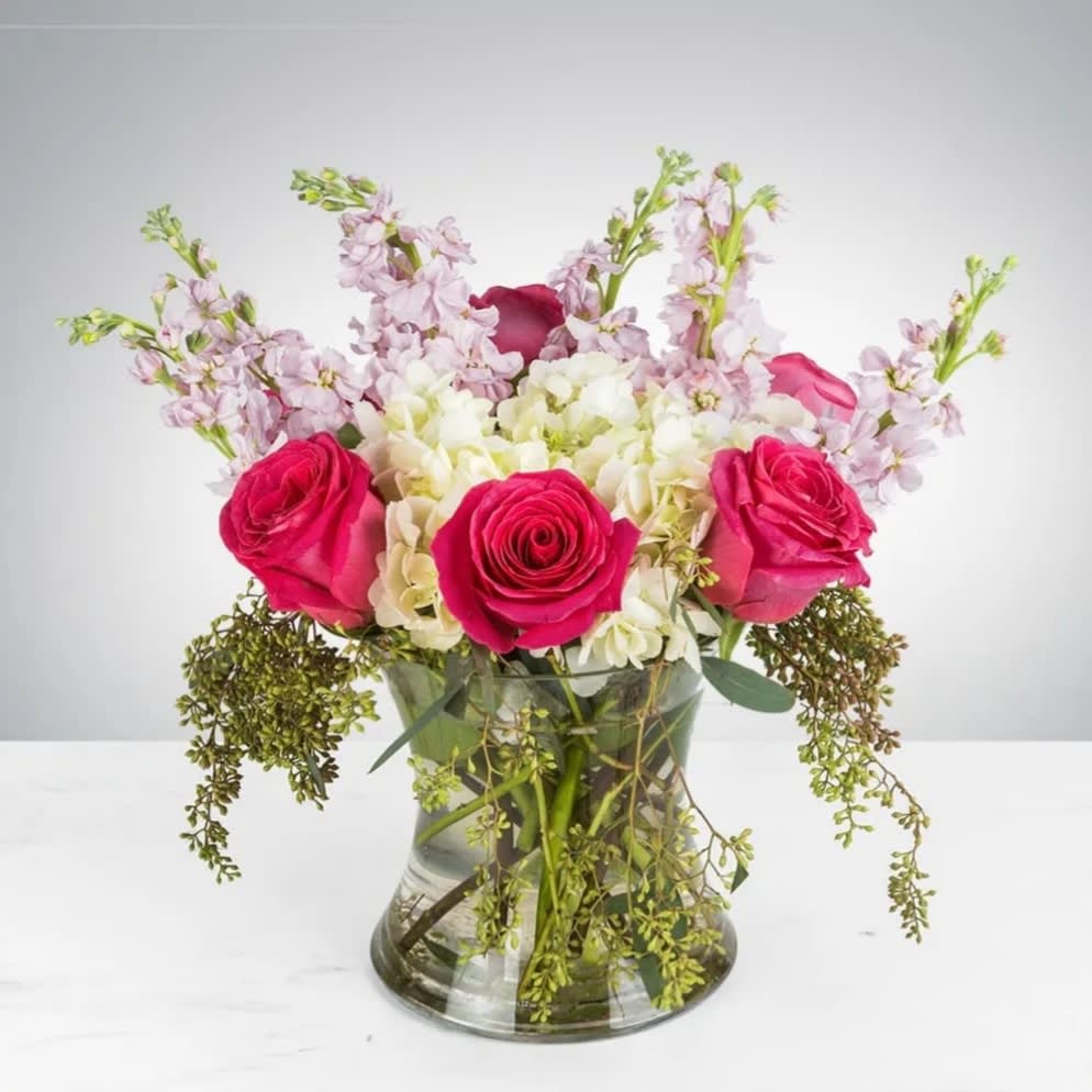 Pink roses and pale flowers arranged in a clear glass vase