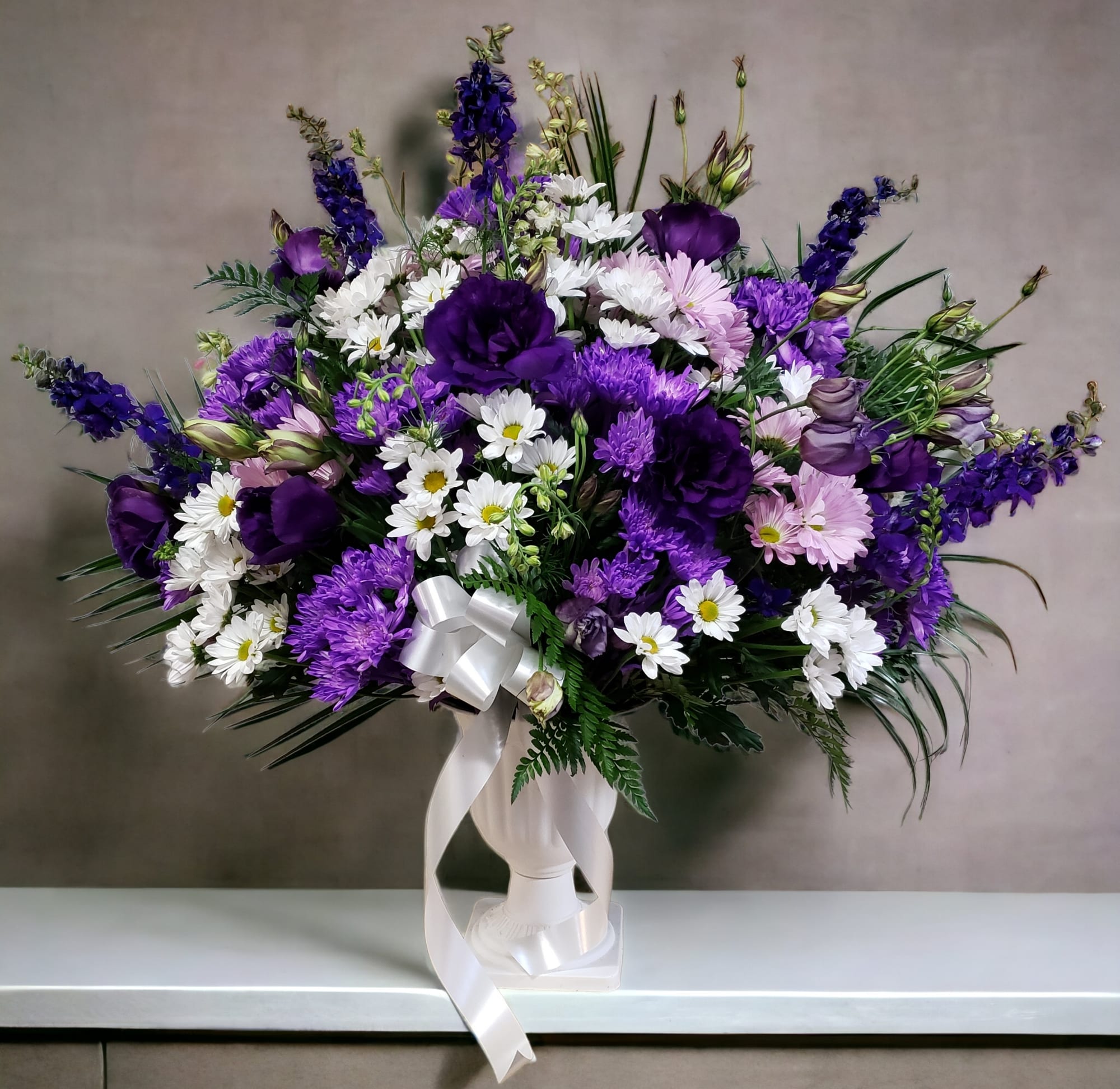 Purple and white mixed flower arrangement in a white vase with ribbon