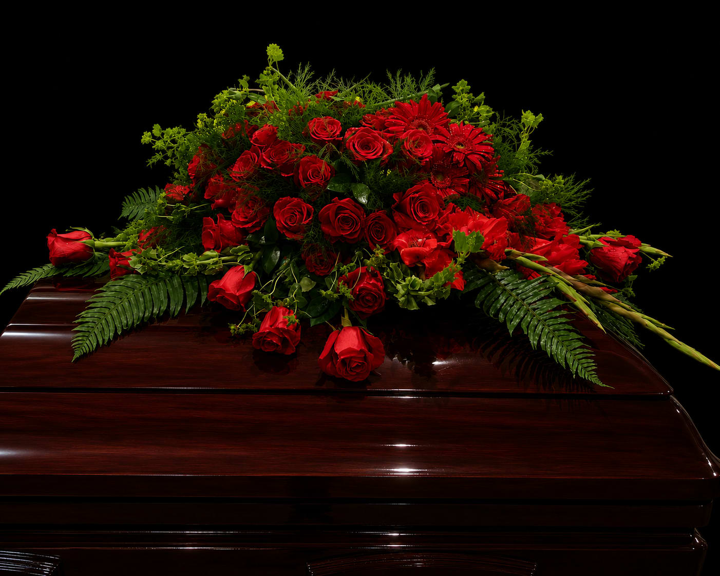 Red rose casket spray with greenery on a dark wood casket
